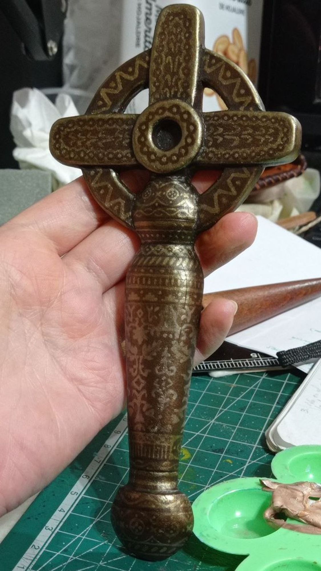 Pic of the cruciform sword handle (from the series Warrior nun) made in leather, with several layers glued and sanded together to make a realistic volume, and painted in shades of silverly bronce with a lot of little decorations along all the piece. 18 cm long