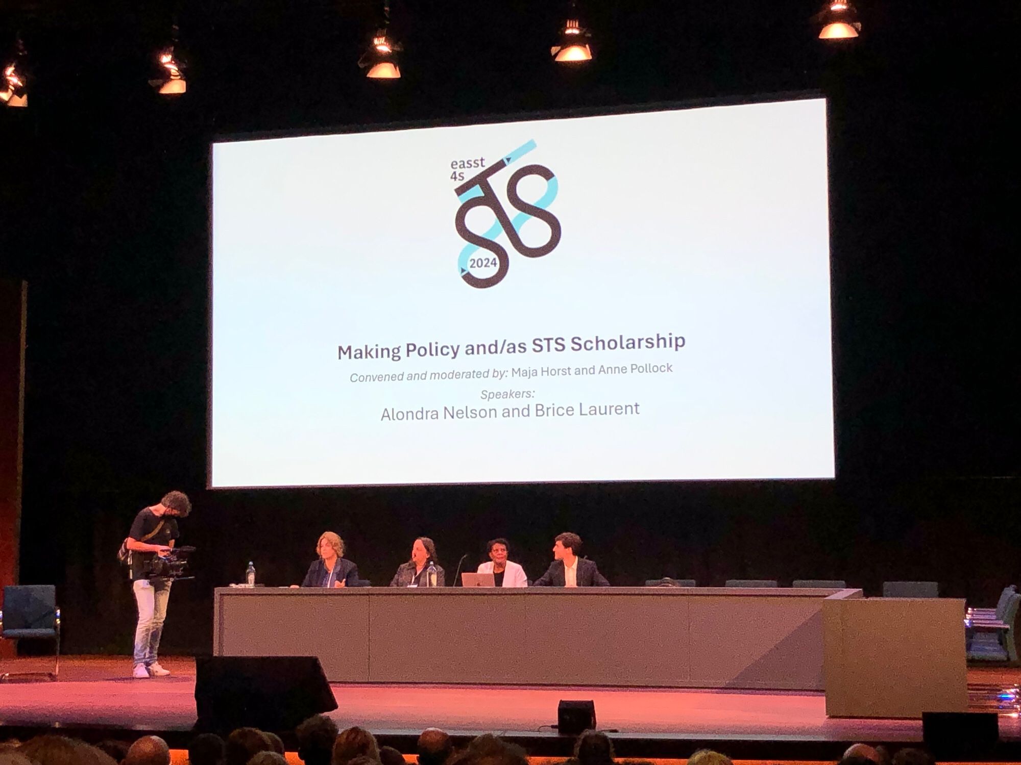 A stage at the EASST 4S conference. Five people on stage, left to right : A camera person, Maja Horst, Anne Pollock, Alondra Nelson and Brice Laurent. A slide in the background saying: Making Policy and/as STS Scholarship.