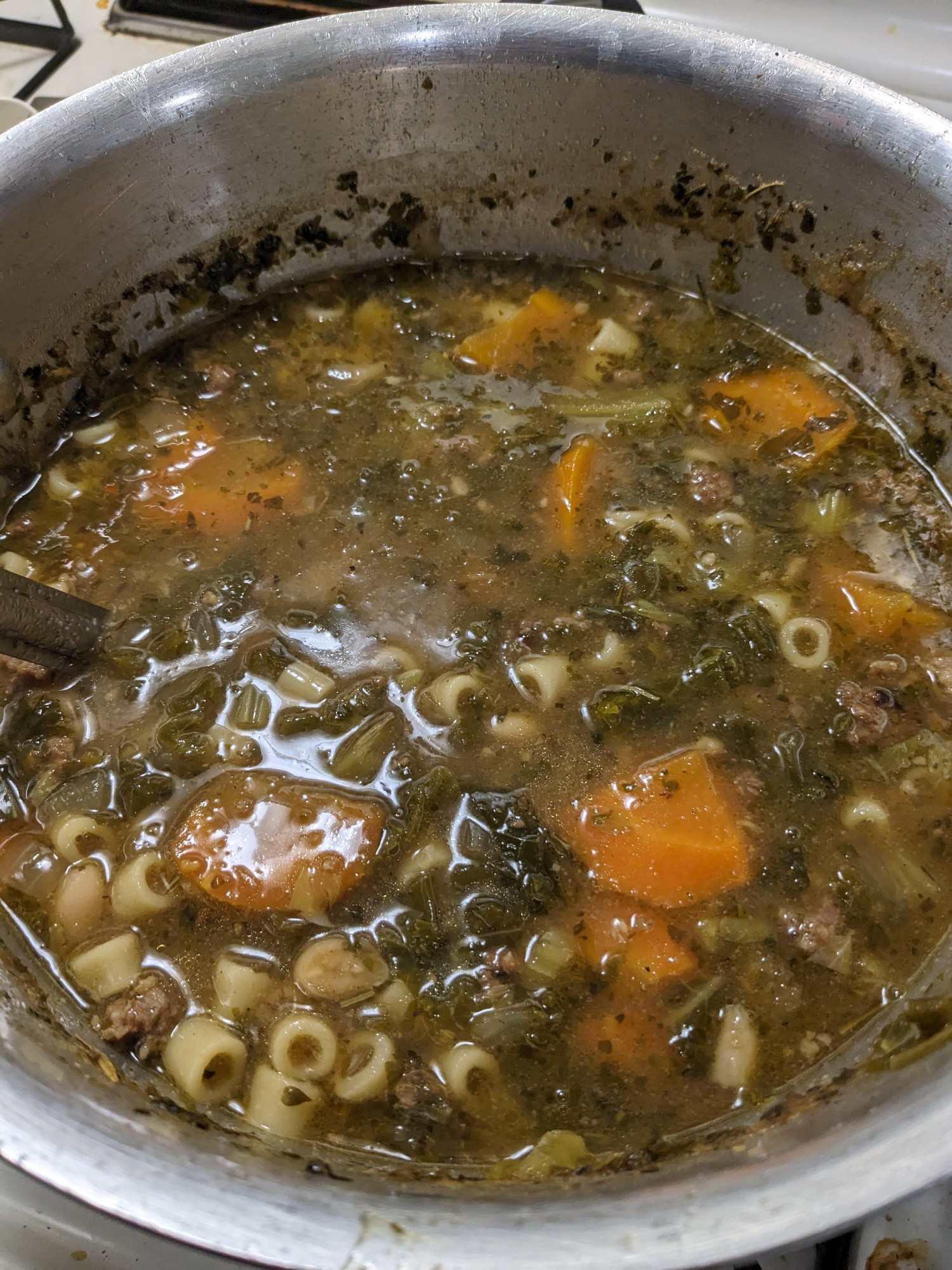 An aluminum pot full of soup, herbed broth unctuous with homemade chicken stock, full of carrot obliques, chopped kale, white beans, and ditalini noodles. 