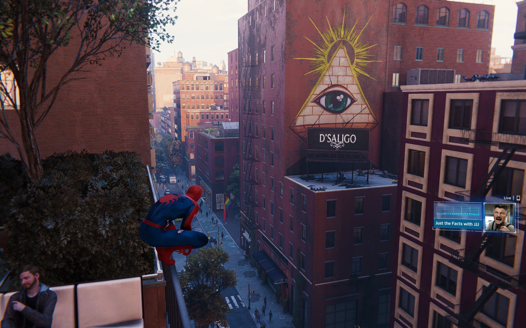 Screenshot from the remastered version of Marvel's Spider-Man. Close to the camera is Spider-Man chilling on a fence. Next to him is a bush and a tree on a mid-sized building in New York. Right in front is a larger building with a giant decal of a pyramid with a green eye on it. It has a golden halo on top. All the buildings have an iconic, red, old brick look. In the middle of the shot there is a pride flag and below it lots of people walk on the street. The light scenario is day, while strong ambient occlusion darkens the buildings in front.