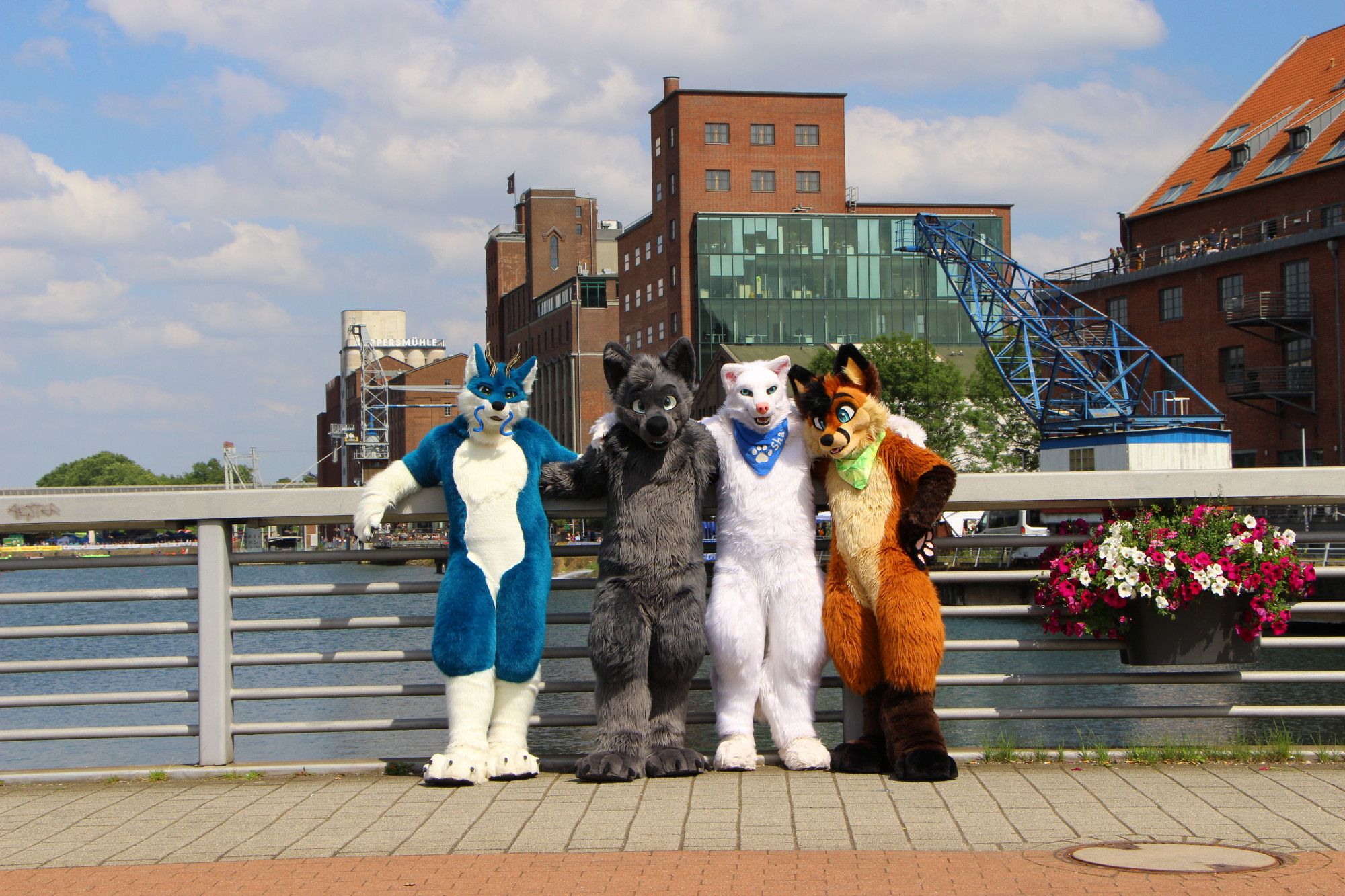 Talles, Quarzar, Shane and Cookie standing on a bridge in front of industrial buildings in the Innenhafen Duisburg.