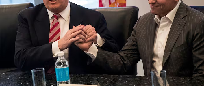 close up of one man with tiny orange hands clearly caressing, not shaking, the closed hand of another man.