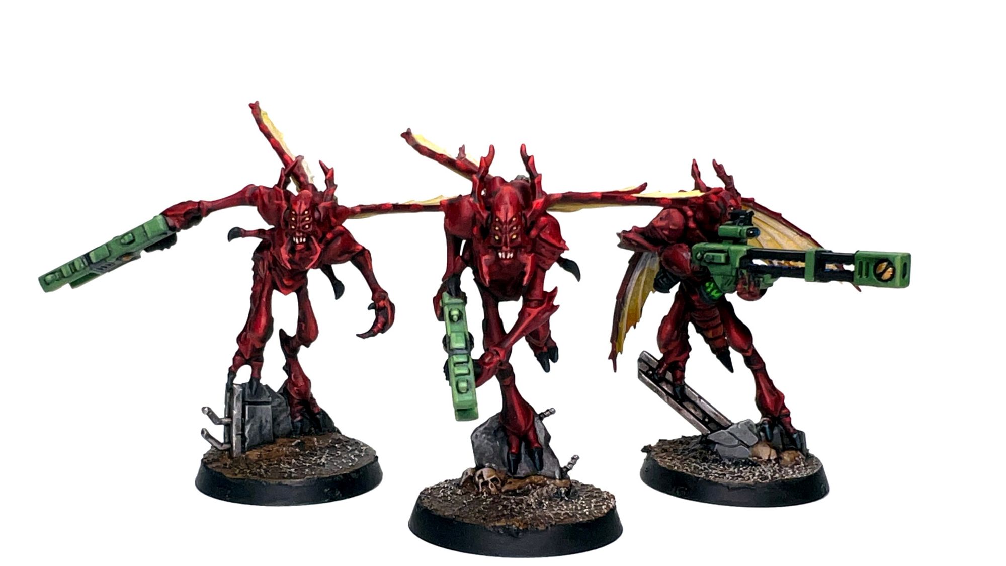 Three Vespid, painted red, with yellow  wings and green wargear. Two Stingwings are on the left and center, with a Longsting (armed with a rail rifle) on the right.