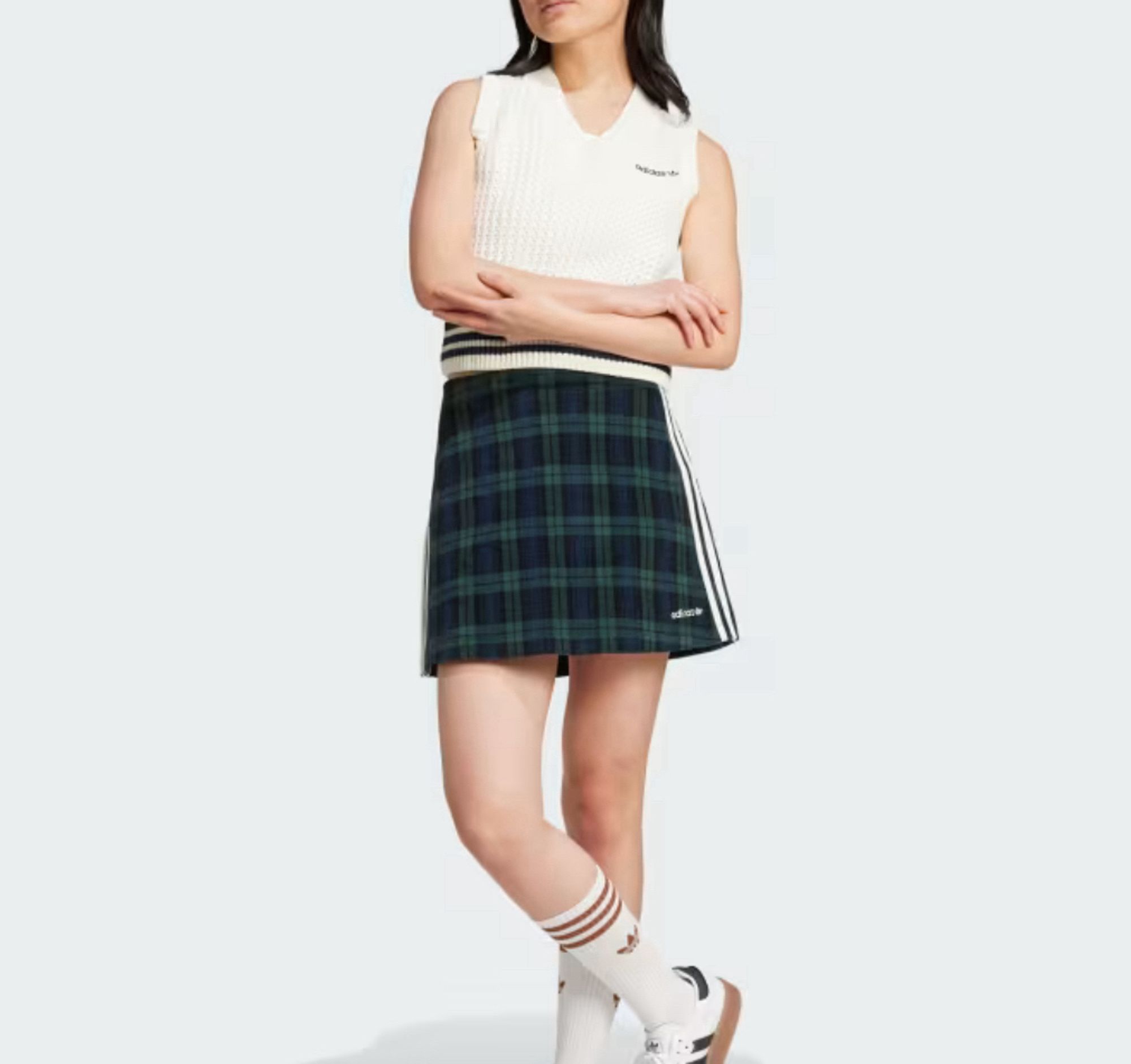 Image of a young woman wearing a green tartan plaid miniskirt with adidas trademark three white stripes along the side. There is a lot of leg showing above white tube socks with red stripes