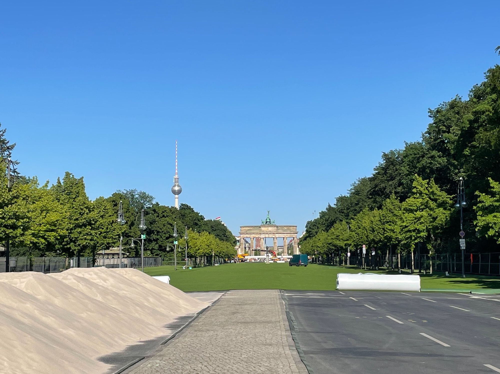 Die Straße des 17. Juni im Berliner Tiergarten, Sicht auf das Brandenburger Tor. Sie ist fast komplett mit Kunstrasen bedeckt worden, eingezäunt. Daneben große Sandhaufen für den Rasen.