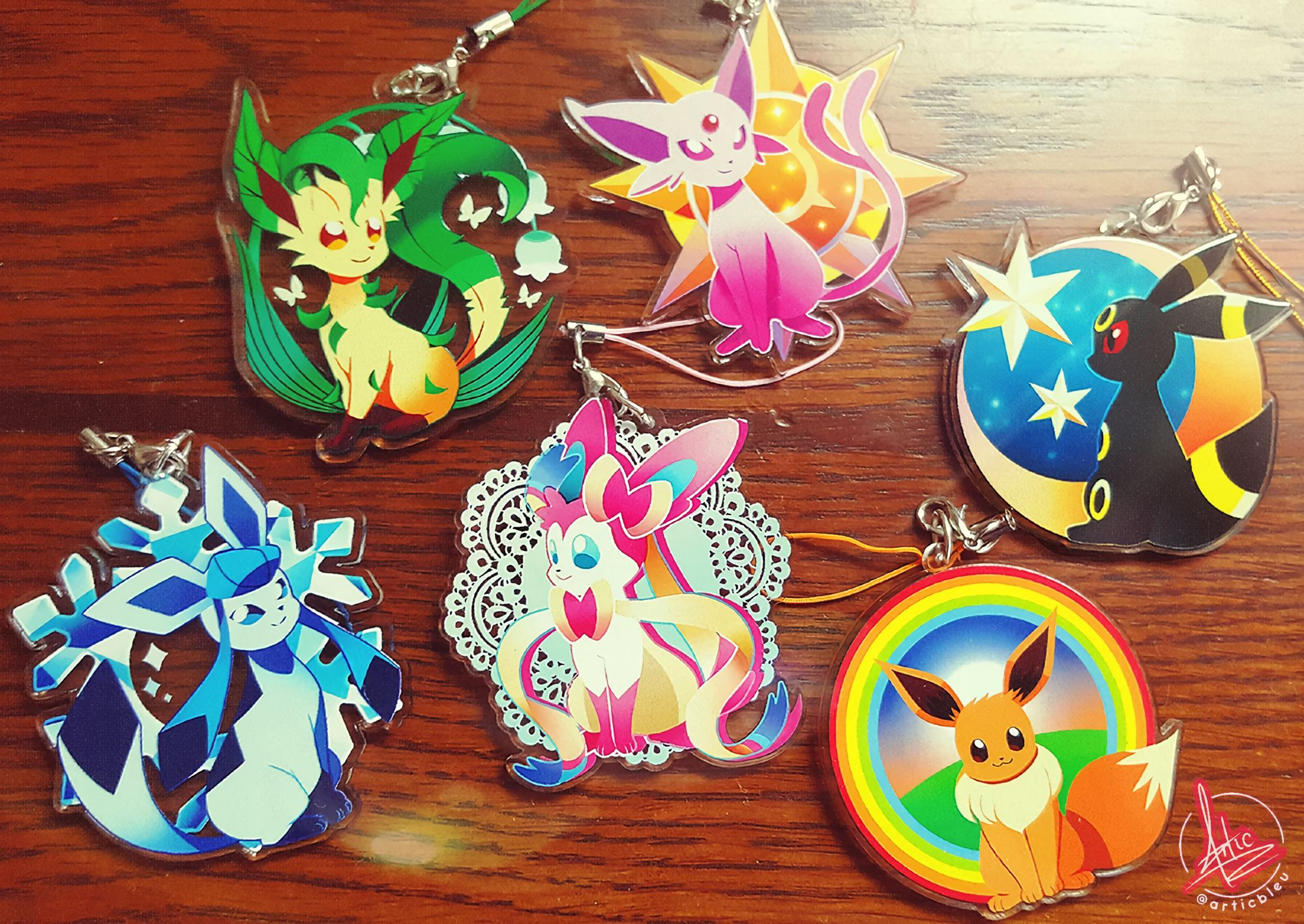 A photo of some Eeveelution acrylic charms, the selection being a Glaceon, Leafeon, Sylveon, Espeon, Umbreon, and Eevee with different circular formats.