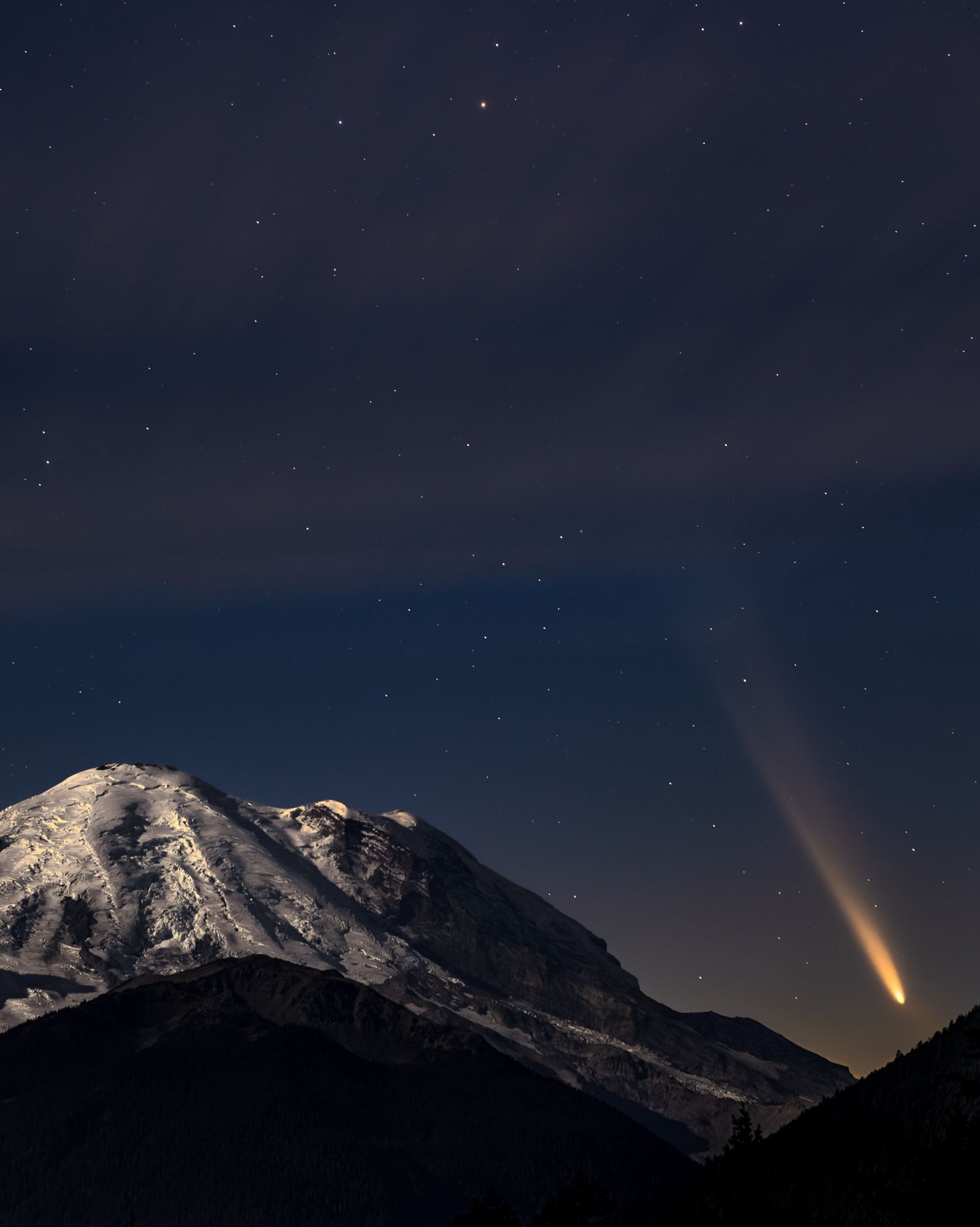 Comet Tsuchinshan sets behind the famous silhouette of Tahoma (Mt. Rainier) as light clouds blur in long exposure overhead