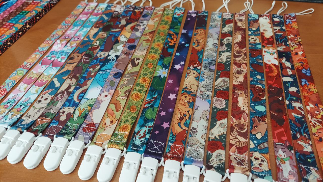 A photo of many pacifier clips lined up side by side. They have bright colorful patterns, including bunnies, kid's blocks, hyenas and foxes.