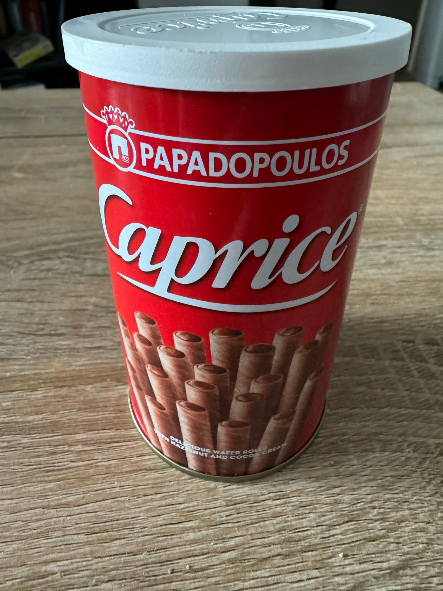 Une boîte de biscuits (des petites gaufrettes en tubes garnies de chocolat) de la marque Papadopoulos. En dessous de la marque est inscrit le nom des biscuits « Caprice »