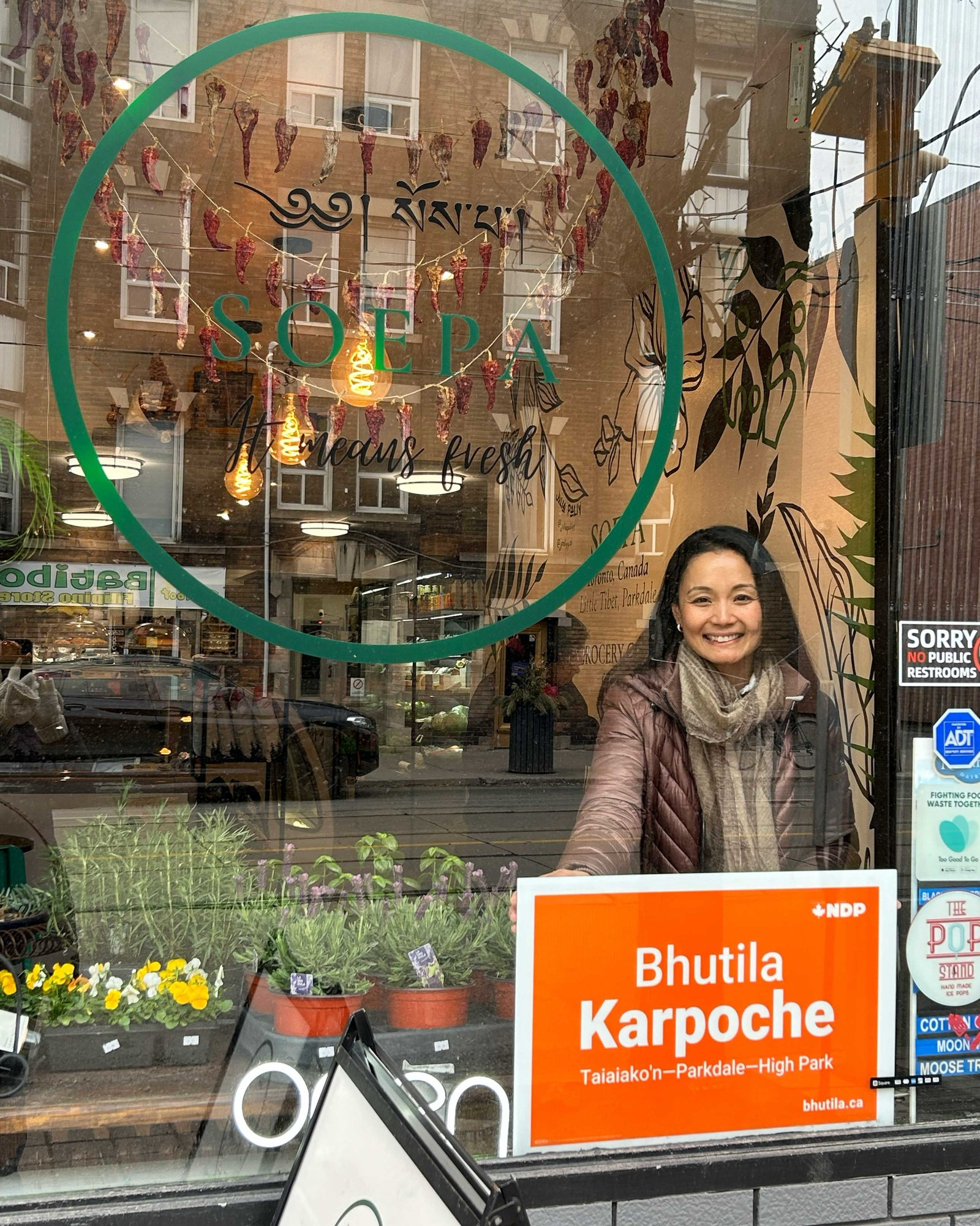 Bhutila Karpoche putting up an election sign in the front window of Soepa, a business on Queen St W in Parkdale.