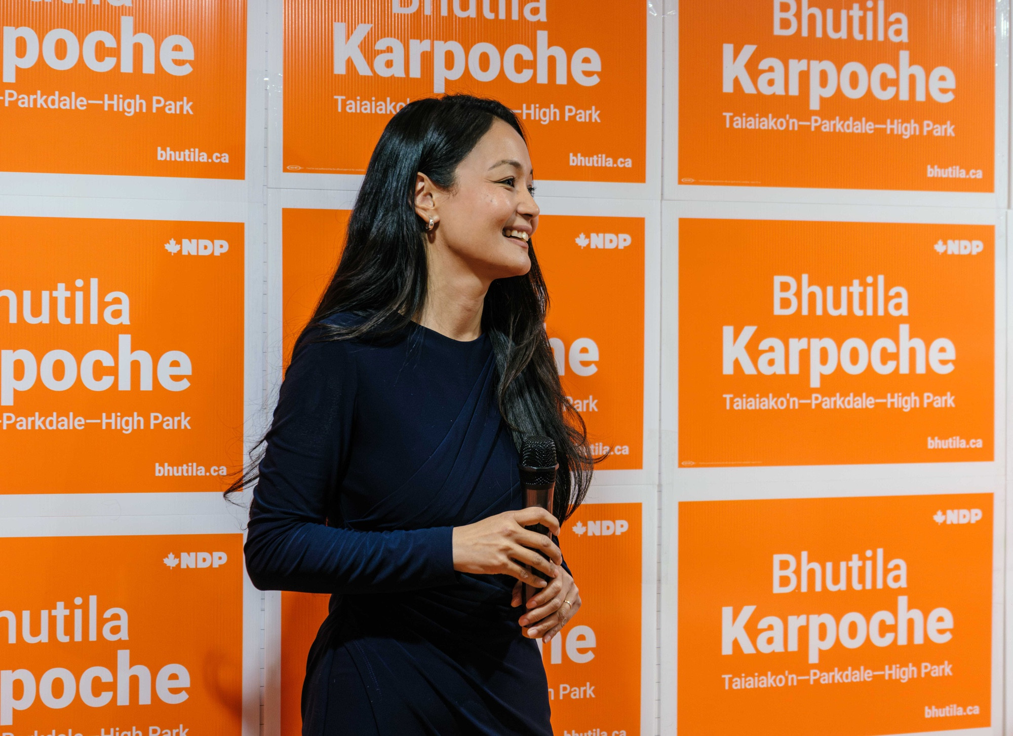 Bhutila Karpoche smiling mid-speech in front of a wall of her election signs.