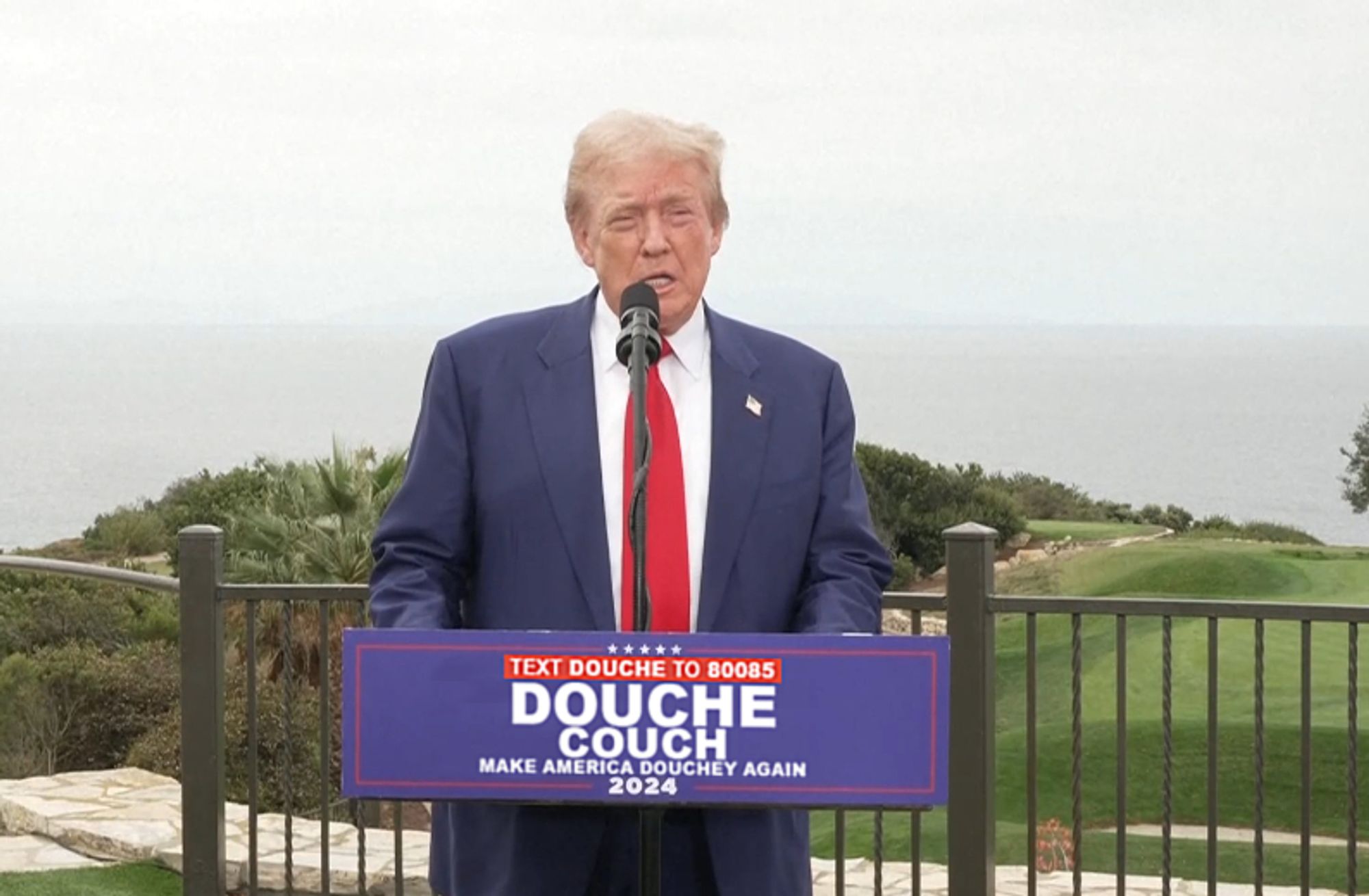 Trump behind a podium photoshopped to say "DOUCHE COUCH" instead of "TRUMP VANCE".