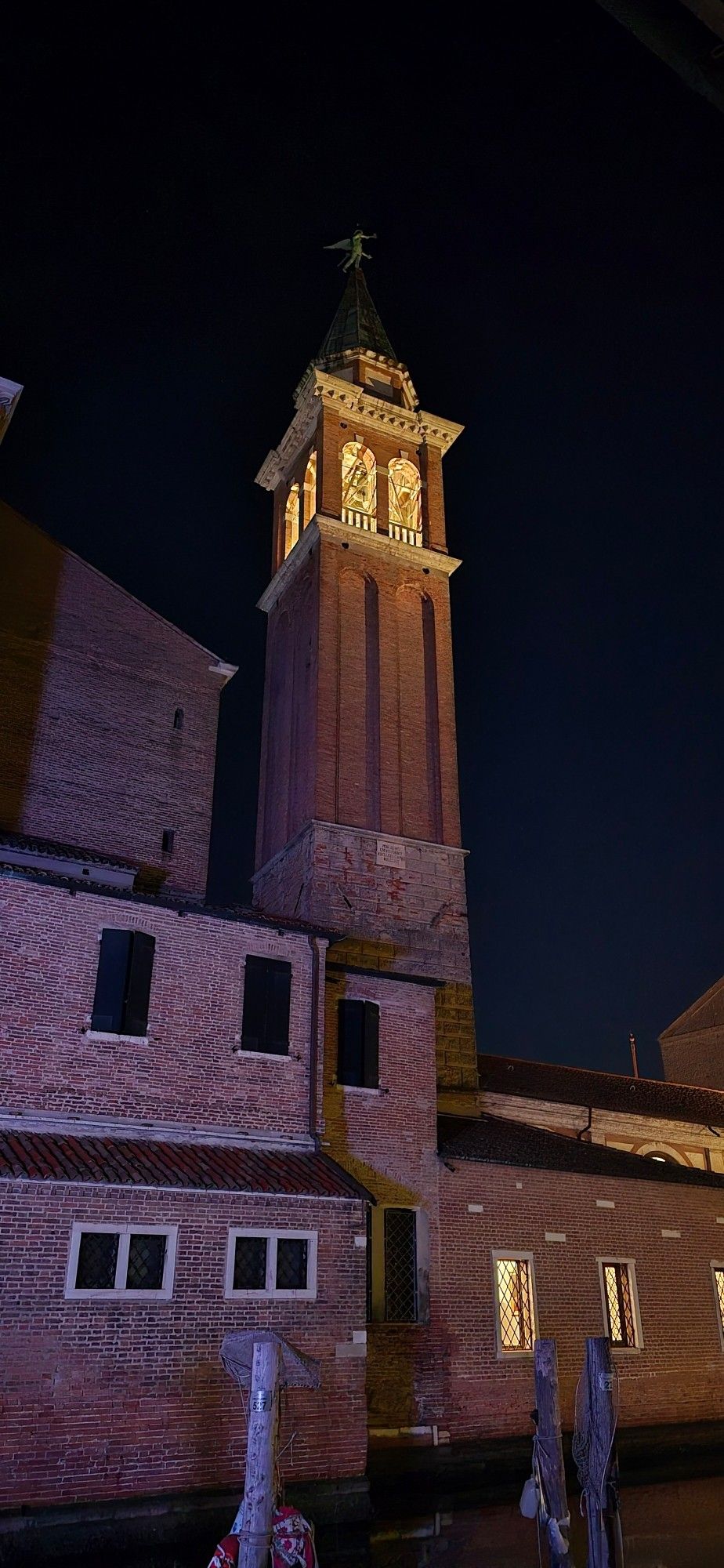 Glockenturm der Kirche von San Giacomo und Santissima Trinità
Ein eckiger Turm aus Backstein mit beleuchtetem Glockenbereich