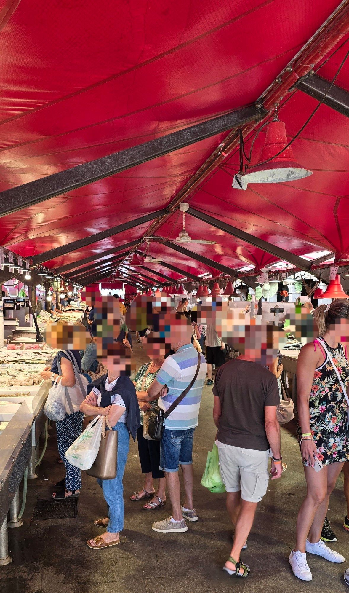 Eine rot überdachte Markthalle mit links und rechts Verkaufsstäbden und vielen Menschen in der Mitte