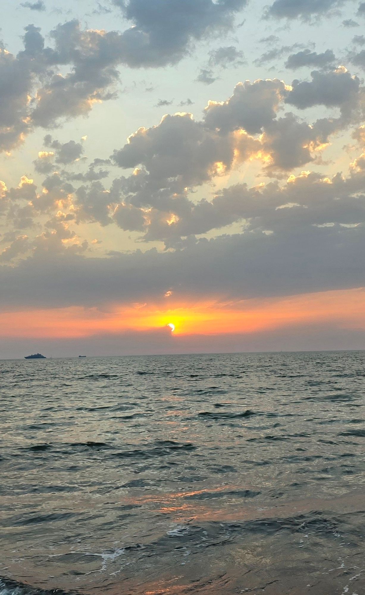 Der Blick übers Meer auf den Horizont mit der aufgehenden Sonne. Hinter einer Wolke lugt eine Ecke der Sonne hervor.