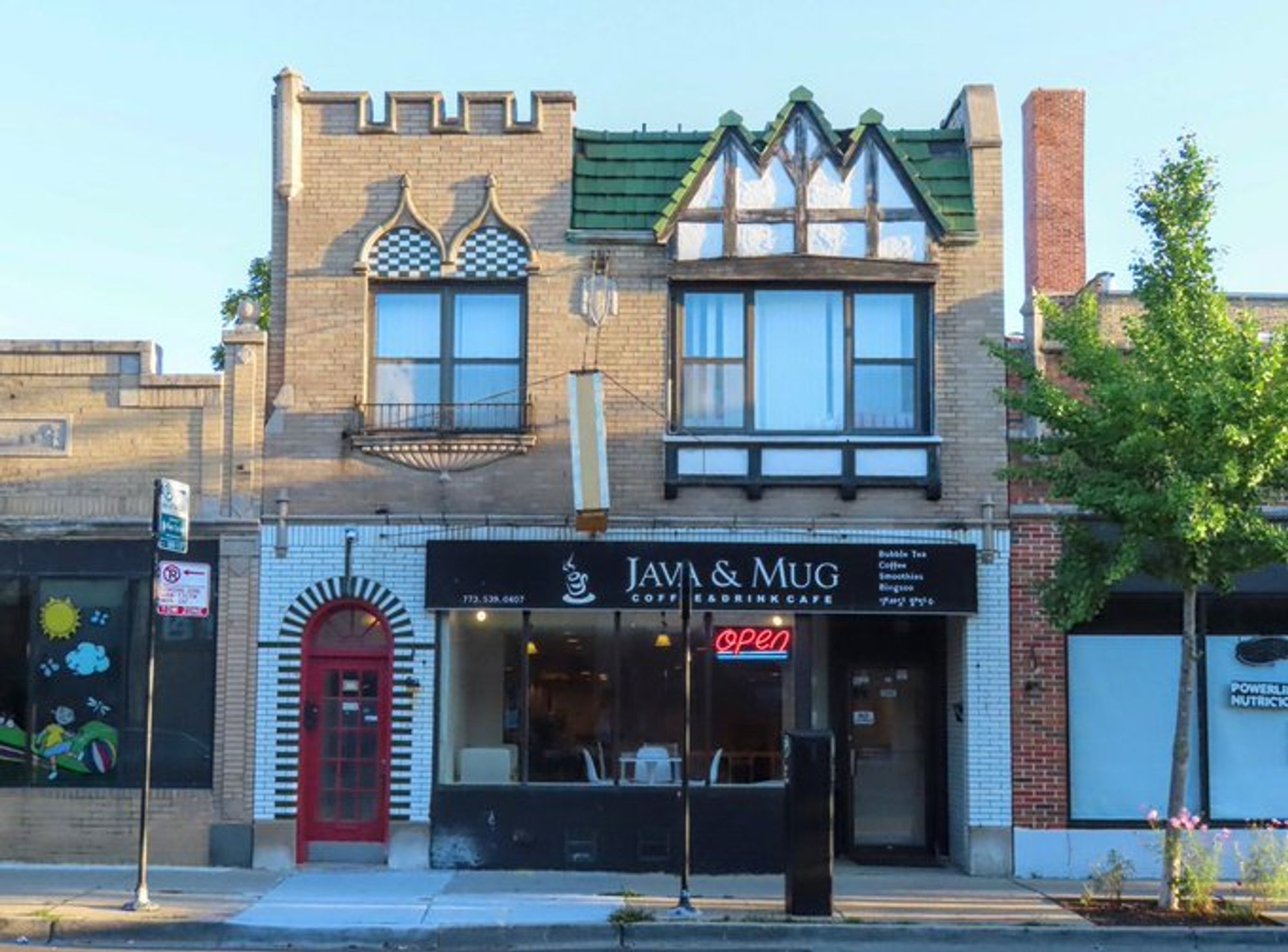 Color photo of two-story building with coffee shop on bottom and apartment on top. Bottom floor is mostly shop windows. Entrance for apartment white glazed brick with green pattern around door. Second floor a riot of details: a half-timbered bay behind a tile mansard roof, castellation and ogee arches over windows.