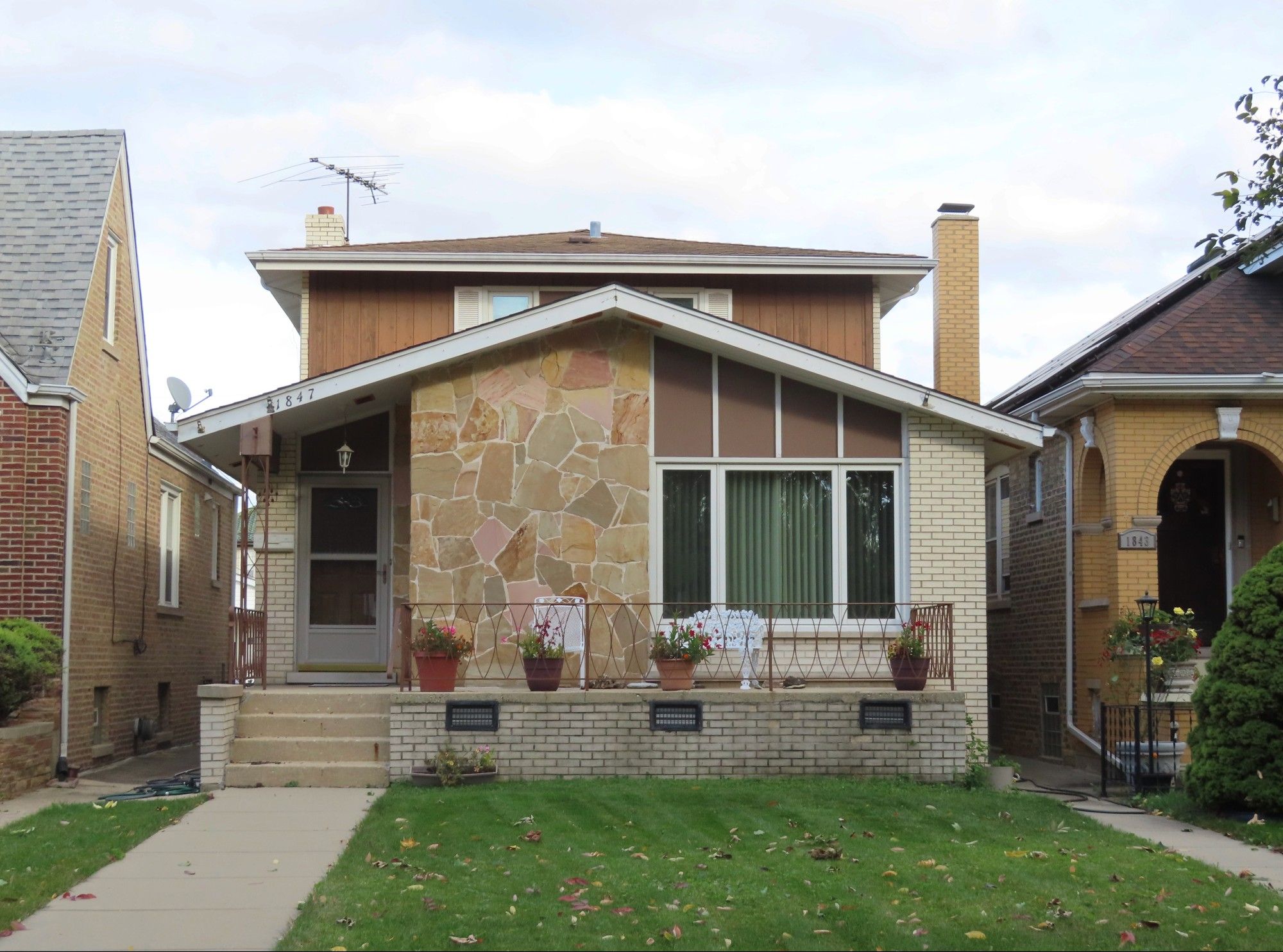 Color photo of one-story building with pop-up looming behind. Front facade is white brick, with large section of flagstone in earth tones and pink.