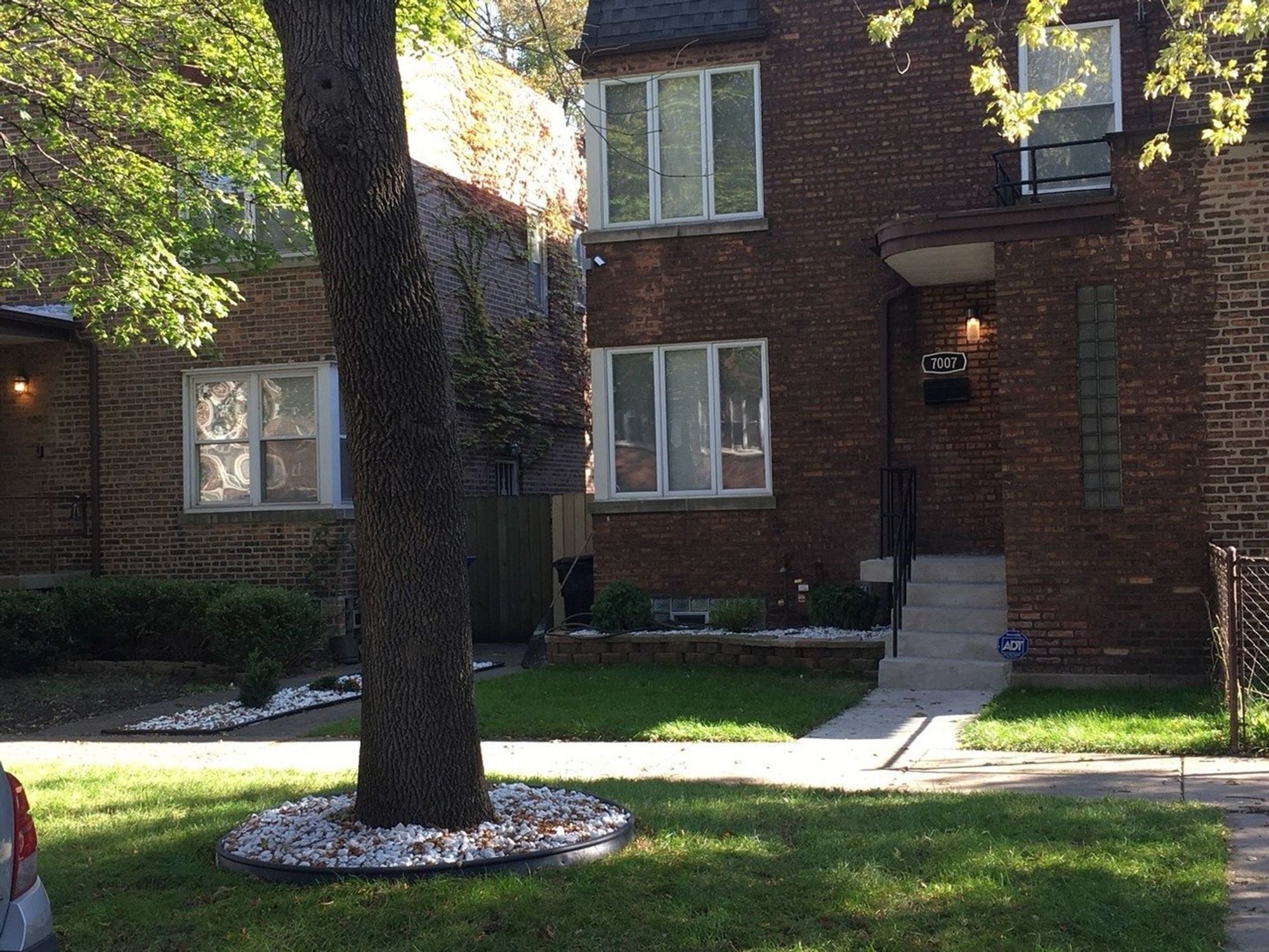 Color photo of entrance to two-story brick building with curved porch roof, with railing above. Glass blocks part of entry bay.