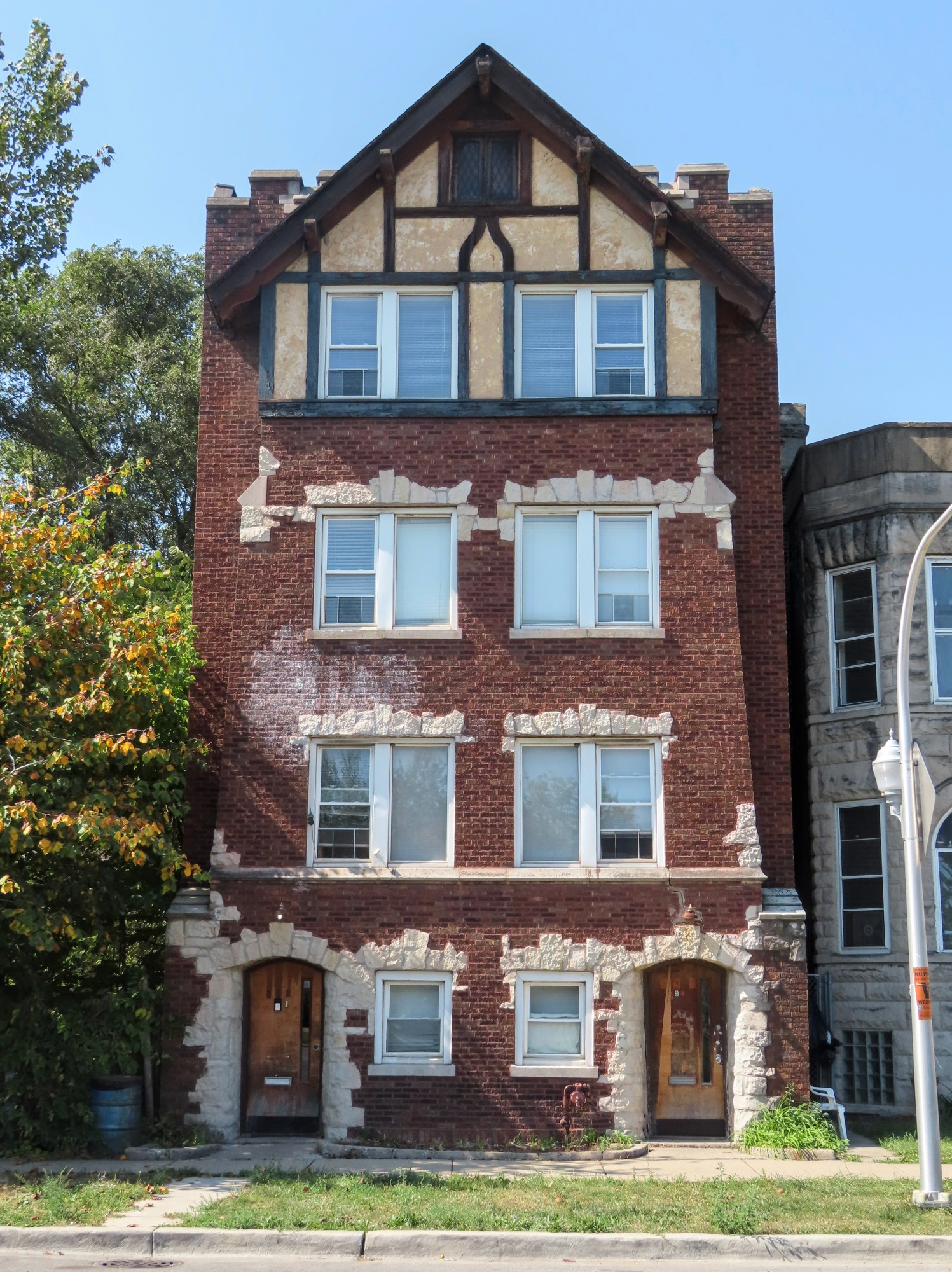 Color photo of four-story apartments building in red brick with flagstone around doors and above windows.  Most of the visible facade is a bay that gets slightly narrower on the second floor-and third floor.