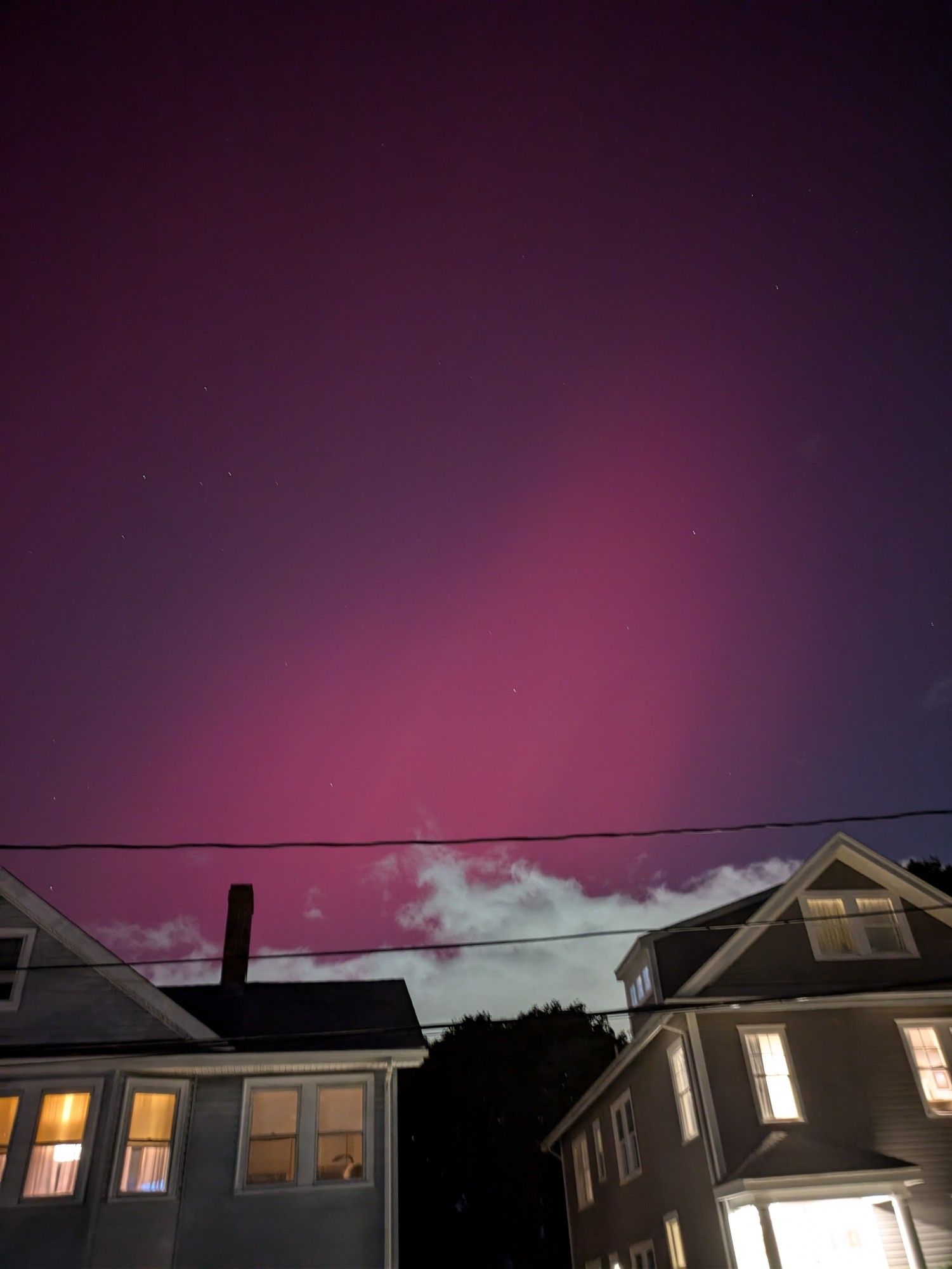 Pink streaks of the northern lights over suburban rooftops, clouds, and trees