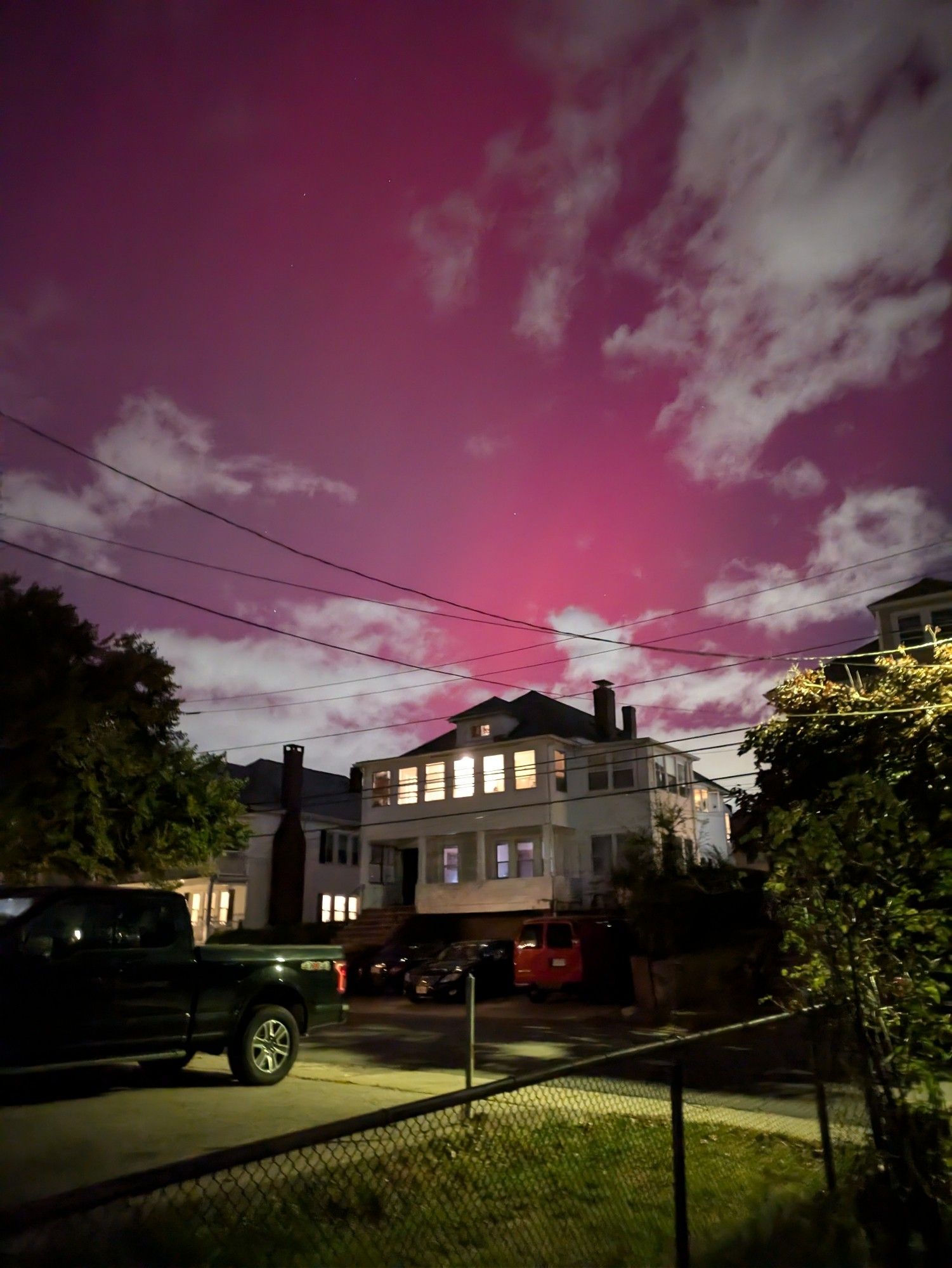 Pink streaks of the northern lights over suburban rooftops, clouds, and trees