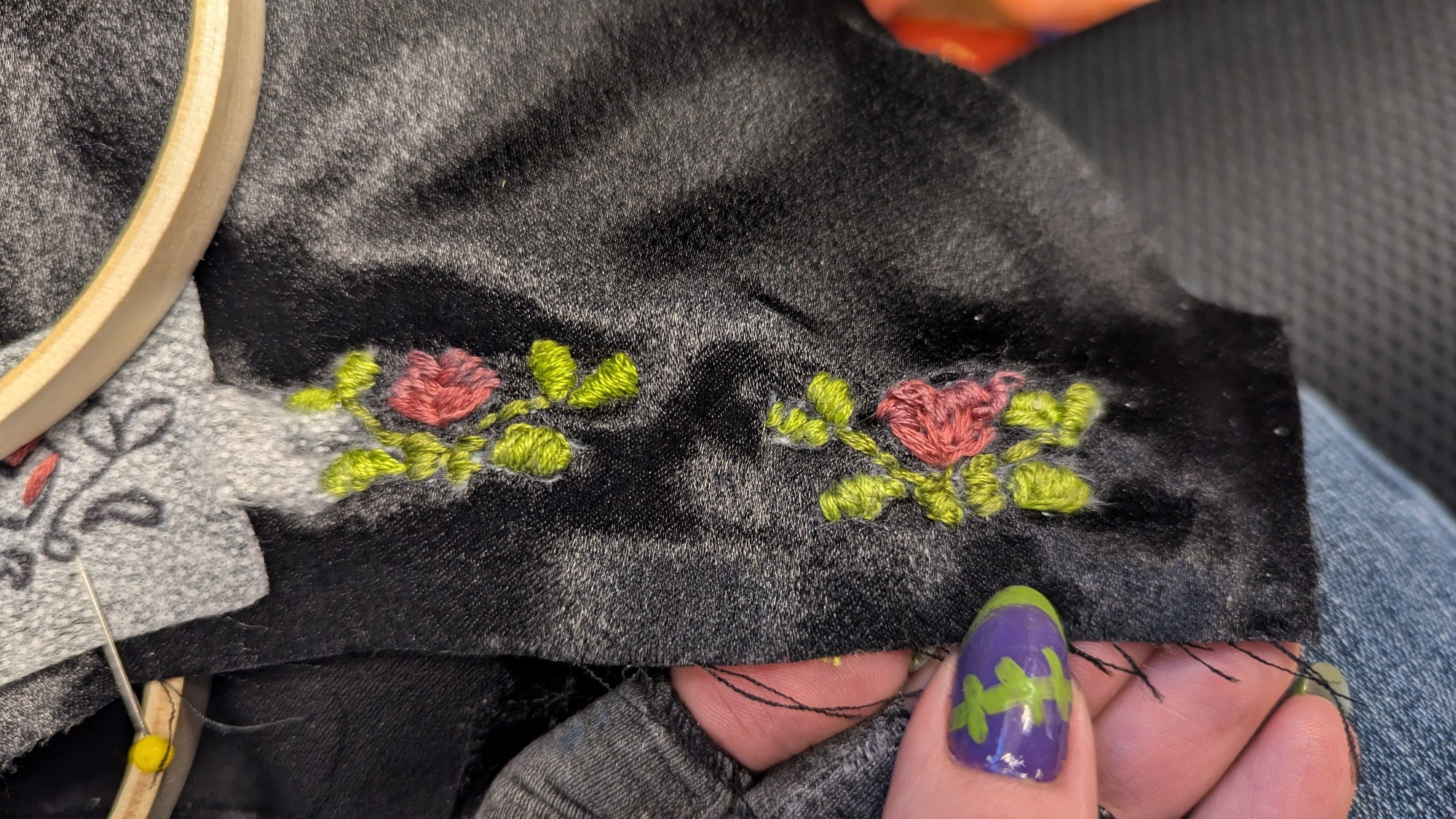 Embroidery of two flowers with leaves on black fabric. The right one is much messier than the left.