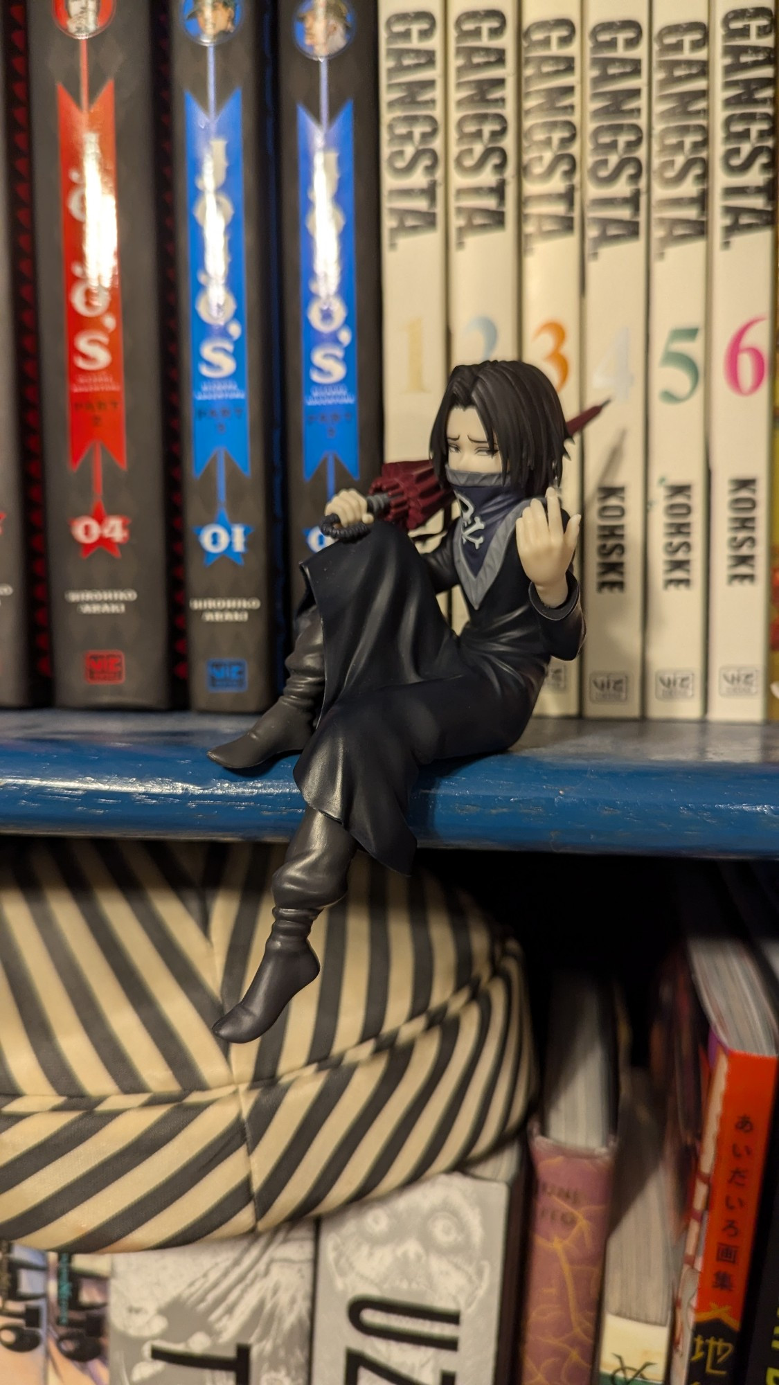 Feitan Hunter x Hunter Noodle Stopper brand figure sitting on a bookshelf in front of Manga.