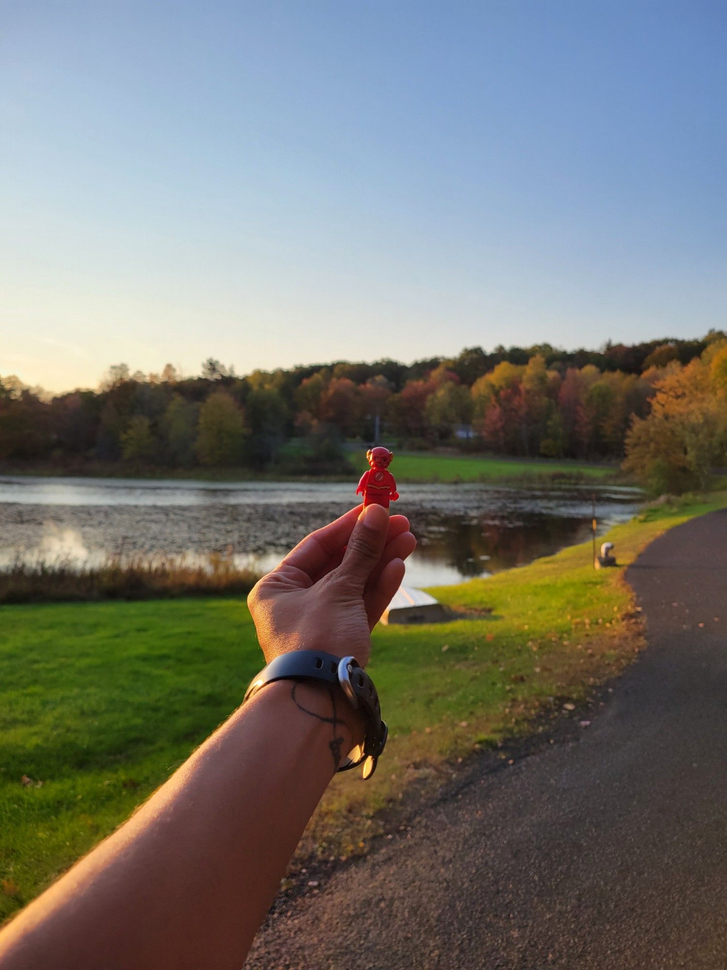 Lego Flash, a Lego mini figure of the superhero The Flash, being held in front of a background of trees and a pond