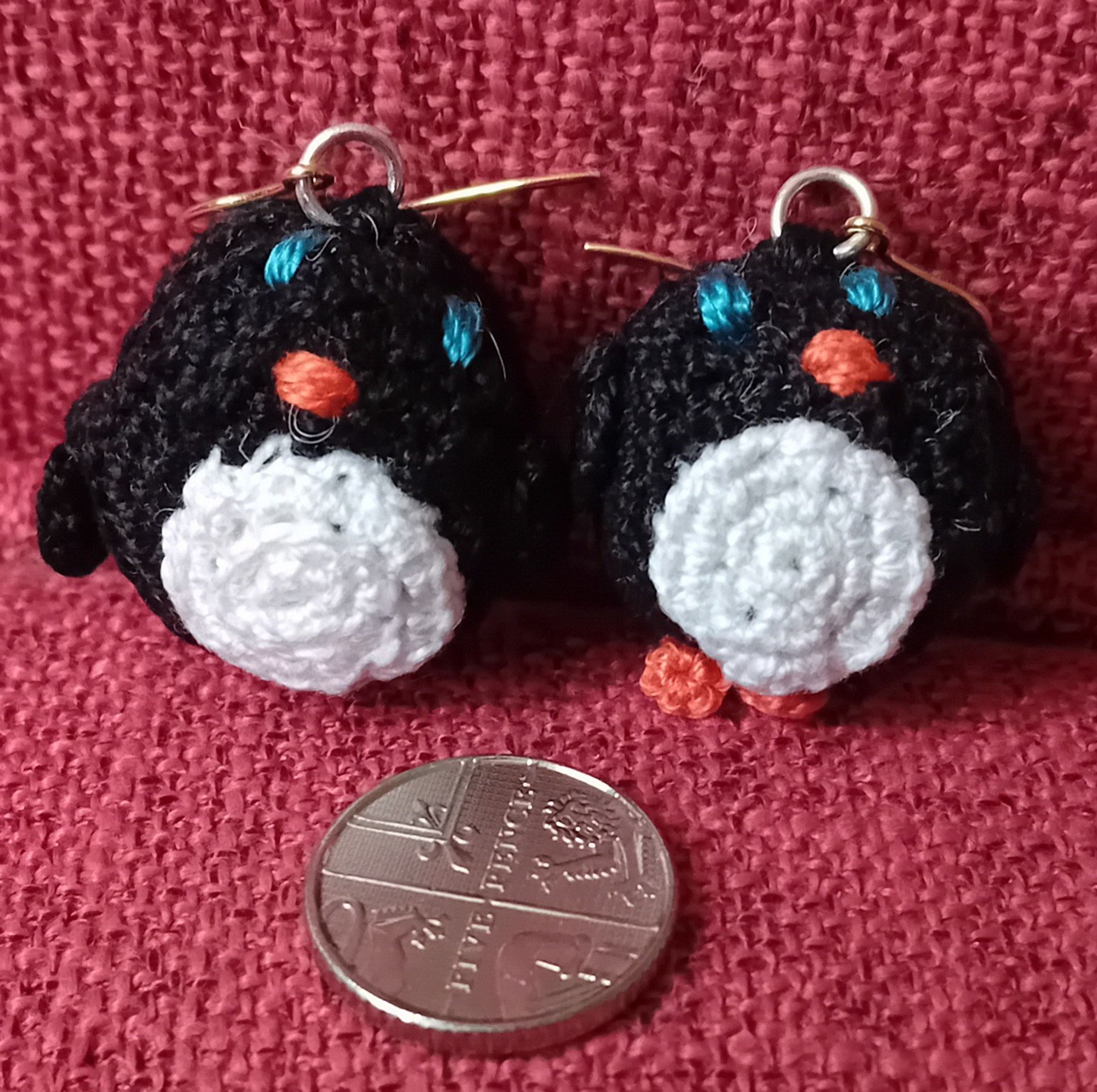 A pair of tiny fat penguin amigurumi crochet earrings, with a 5p for scale