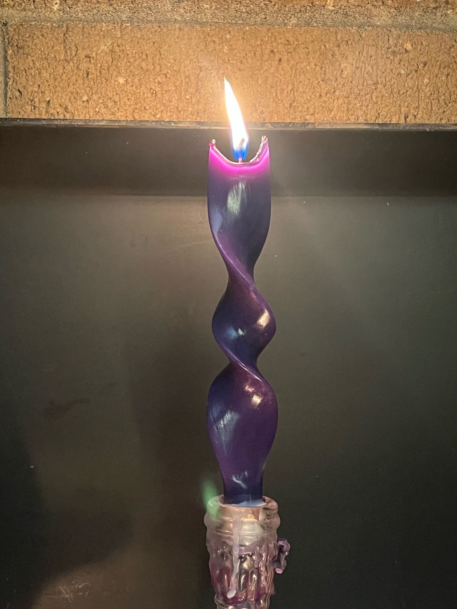 A purple taper candle that’s twisted like a unicorn horn