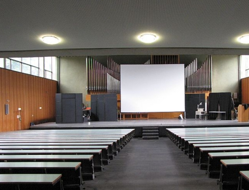 Bühne in einem langweiligen Vorlesungssaal mit Orgelpfeifen hinter der Leinwand.