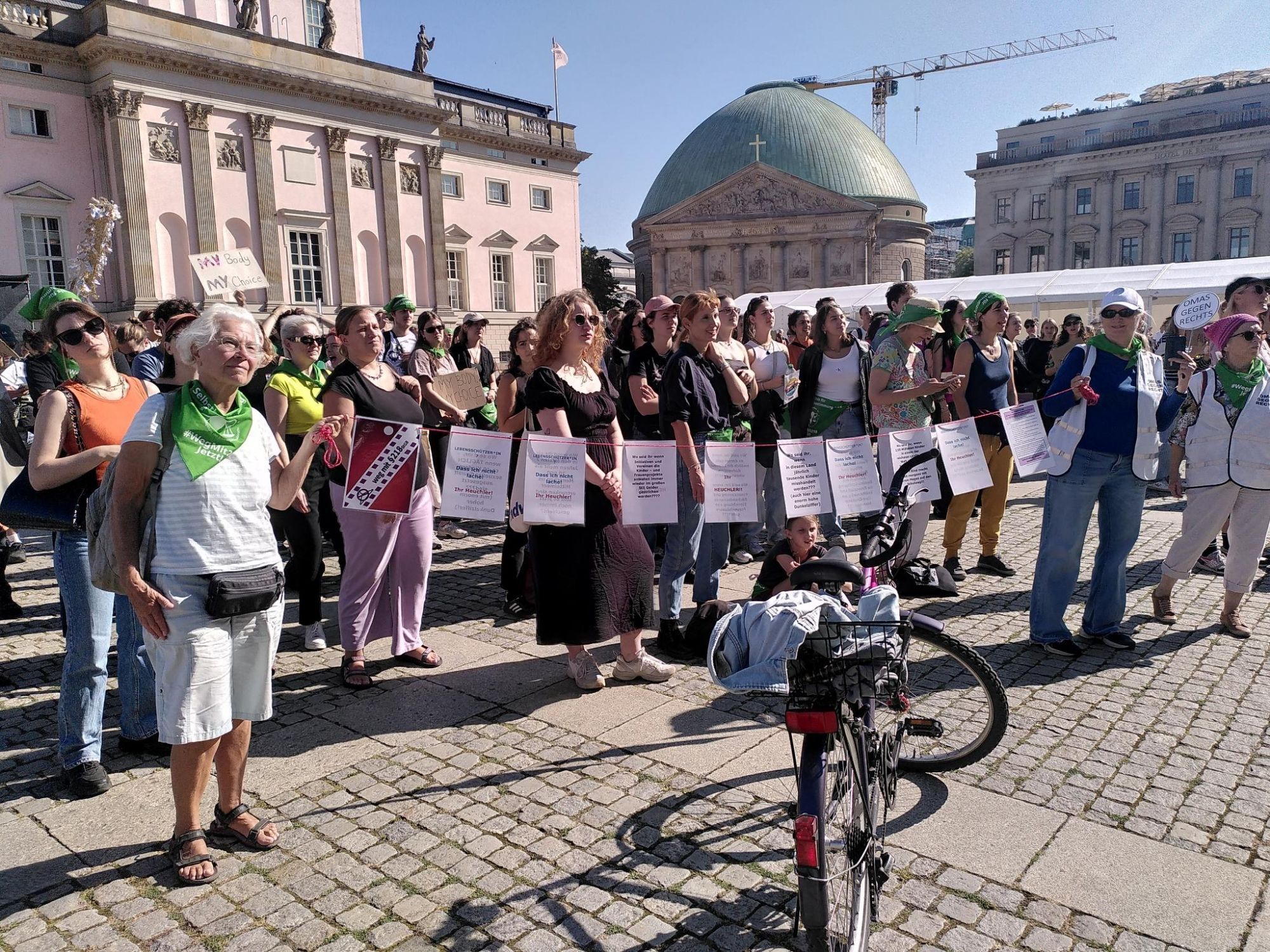 Viele Frauen am Brandenburger Tor mit einer Leine, an der verschiedene Argumente zum Thema Audio A4 Blättern hängen