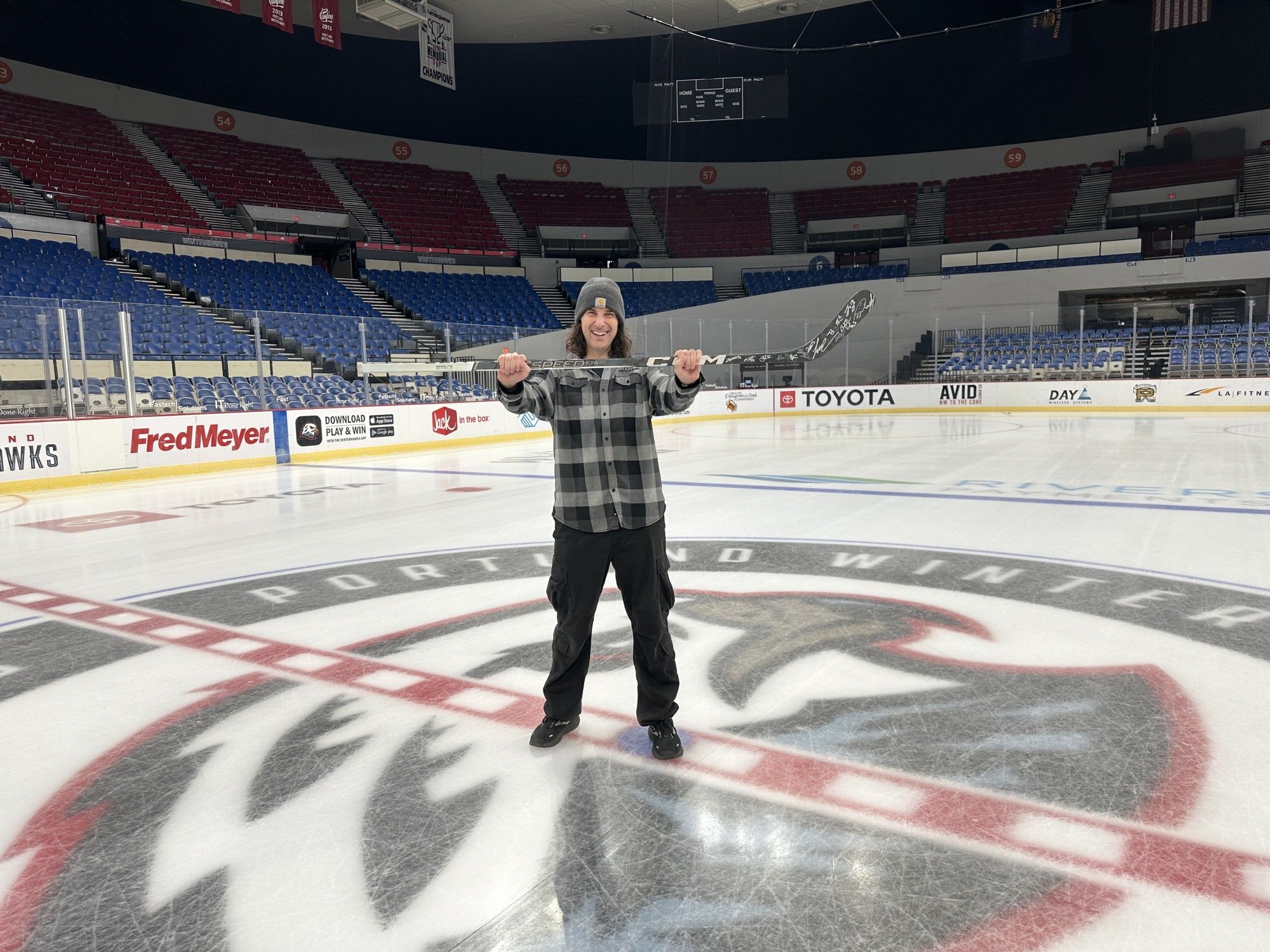 Joe Grand standing on center ice in Portland's Veterans Memorial Coliseum holding a hockey stick signed by the Winterhawks