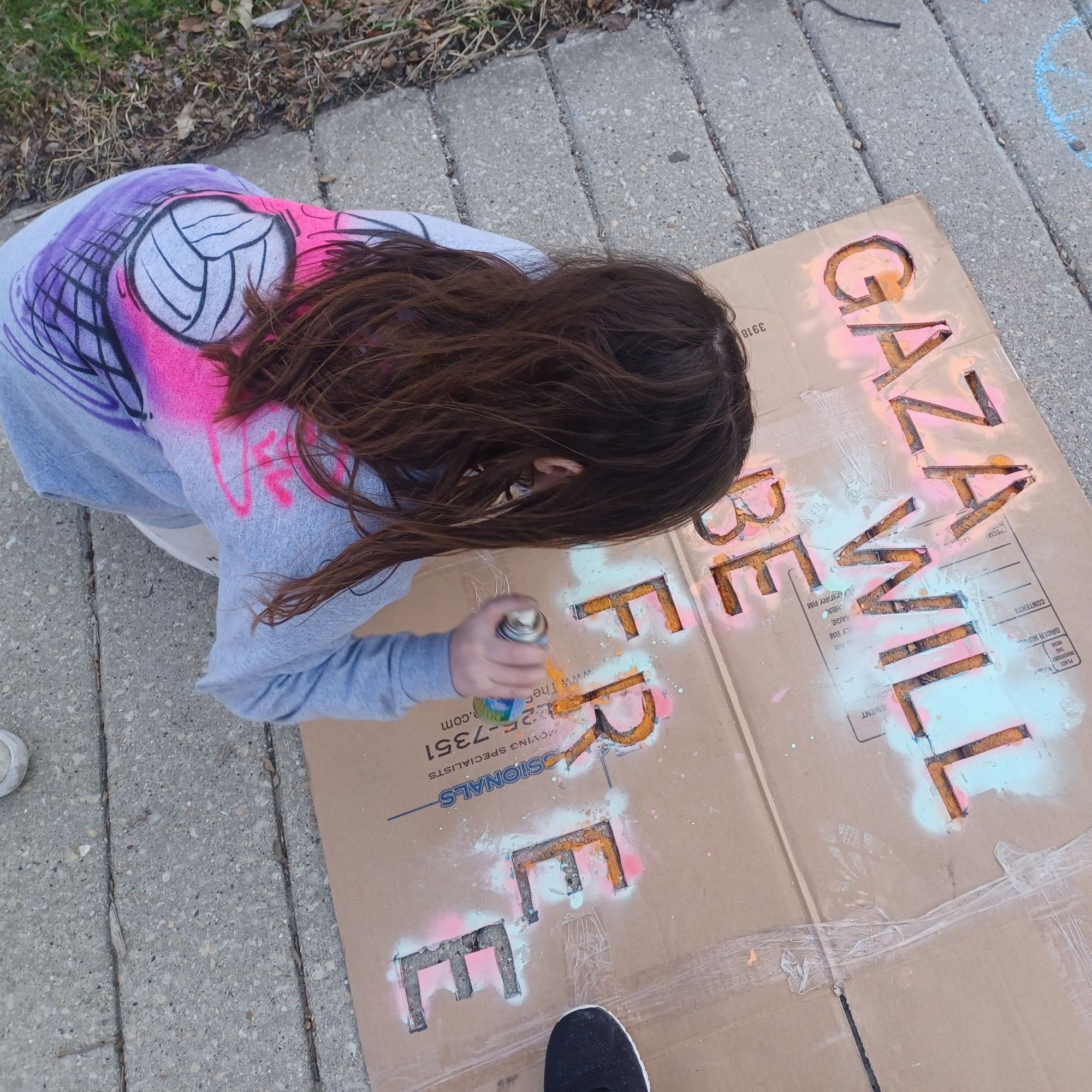 Child uses chalk spray to write "Gaza will be free" on a sidewalk