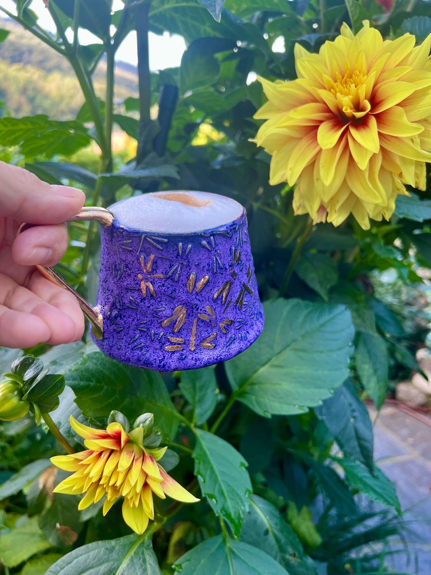 Violette Tasse mit goldenen Libellen zwischen gelben Dahlien