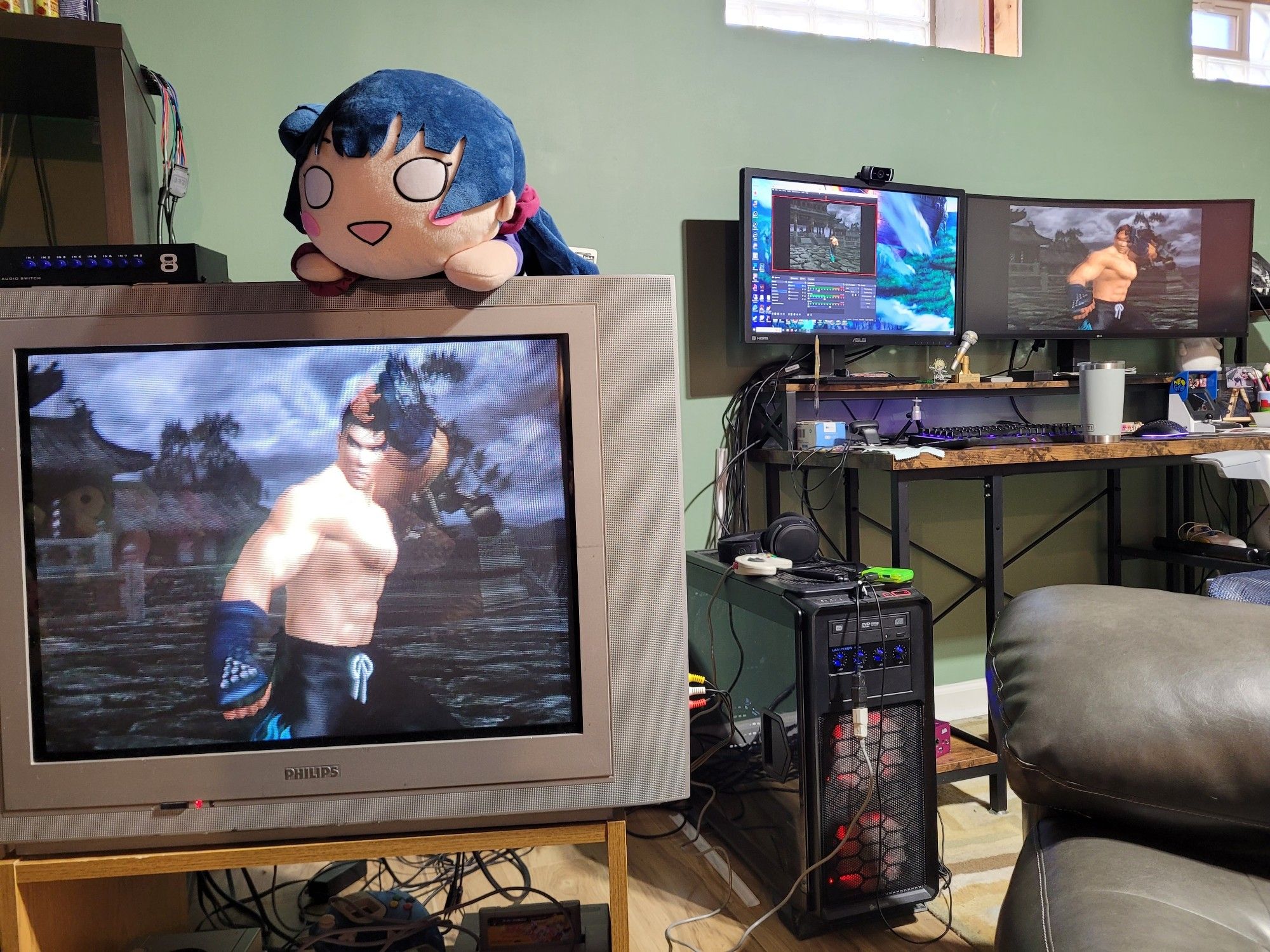 A CRT setup in the foreground with a dual-monitor PC setup in the background. All three screens are displaying Tekken Tag 1. A Yohane plushie sits atop the CRT