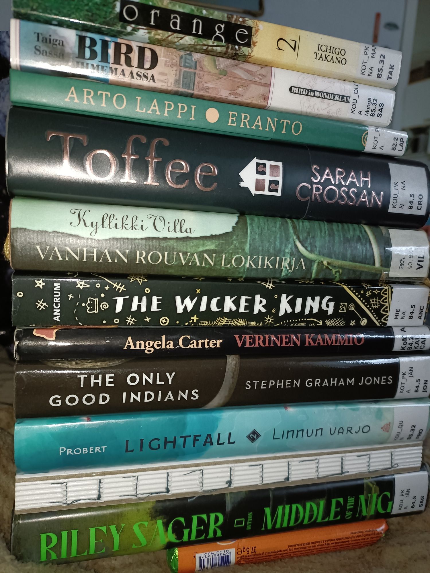 Korkea kirjastolainojen pino. 

Ichigo Takano: Orange 2 
Taiga Sassa: Bird ihmemaassa 7 
Arto Lappi: Eranto 
Sarah Crossan: Toffee
Kyllikki Villa: Vanhan rouvan lokikirja 
K. Ancrum: The Wicker King 
Angela Carter: Verinen kammio 
Stephen Graham Jones: The Only Good Indians 
Tim Probert: Lightfall kirja 2 - Linnun varjo 
Heikki Valkama: Oishii - japanilaista kotiruokaa 
Riley Sager: Middle of the Night 

Pinon alla oranssi mentospötkylä pitämässä sitä pystyssä.