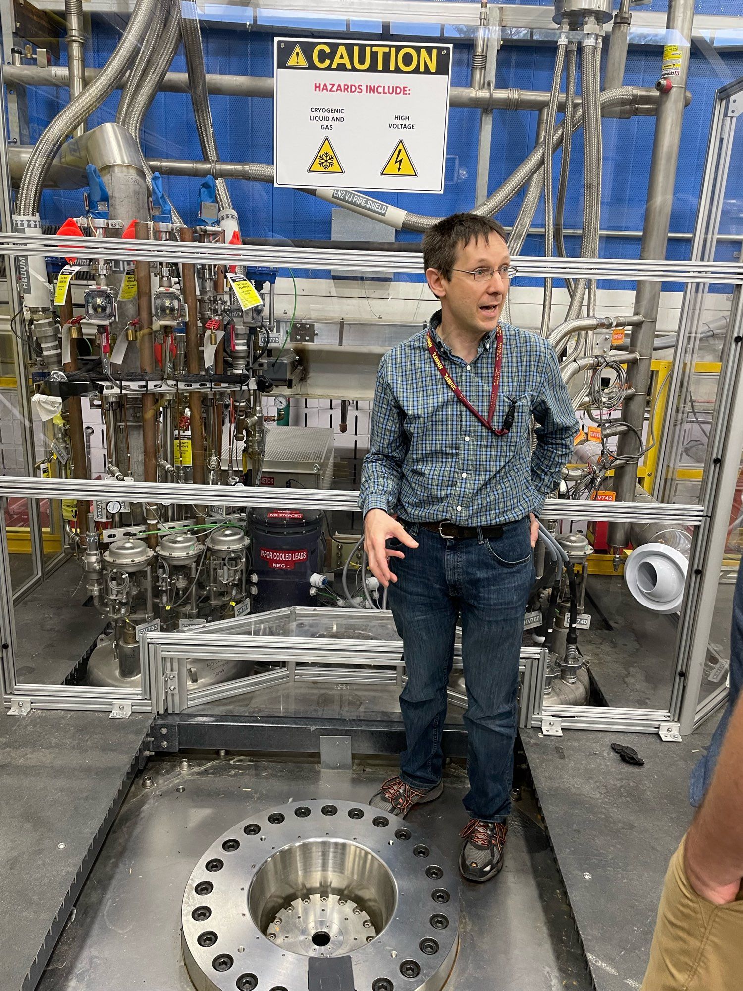 Ilya standing on top of the series connected hybrid magnet. He is on a stainless steel platform in front of a plexiglass barrier with a lot of high power electrical connections behind it.