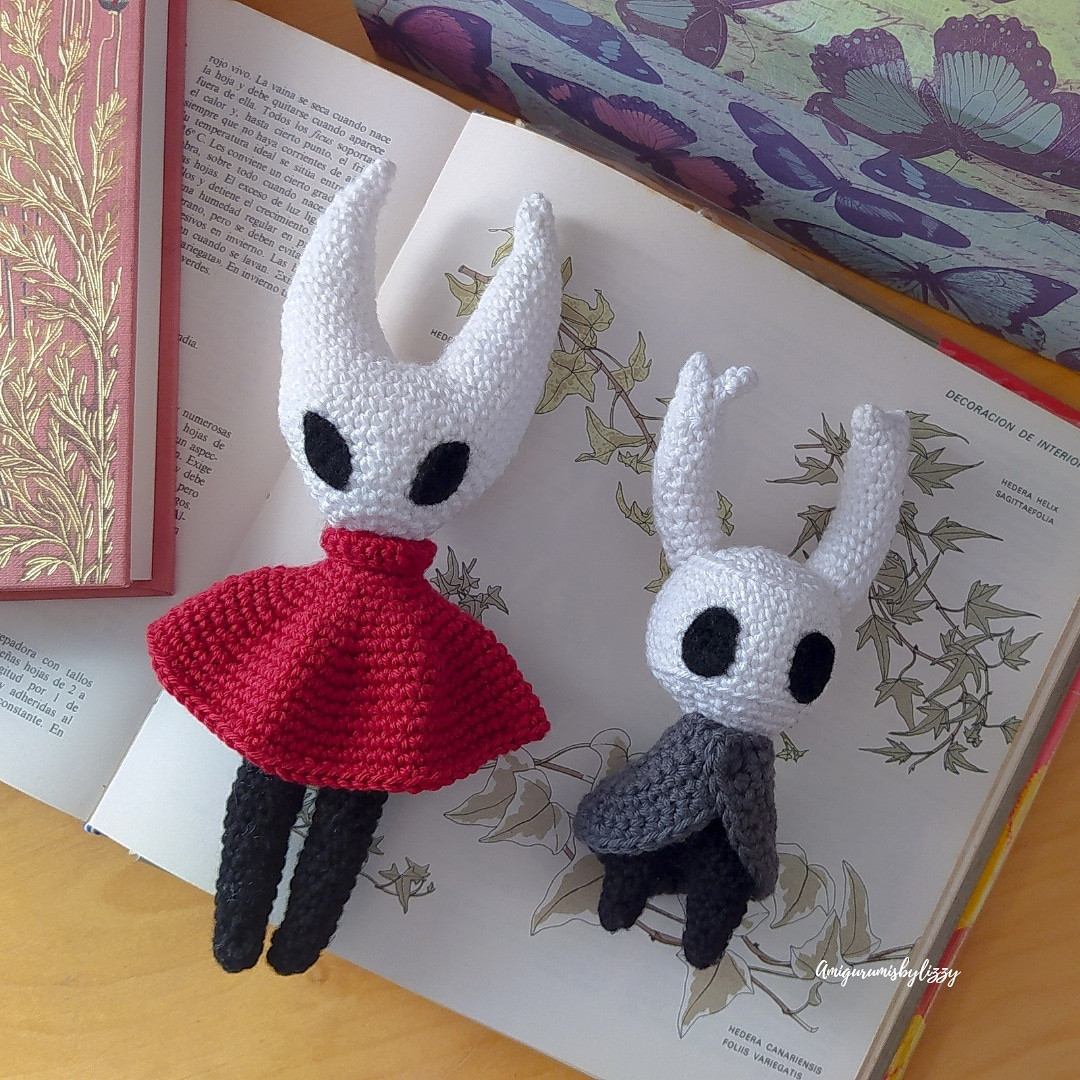 Muñecos de crochet de los personajes de hollow Knight sobre  un libro de plantas abierto y junto a una caja de mariposas