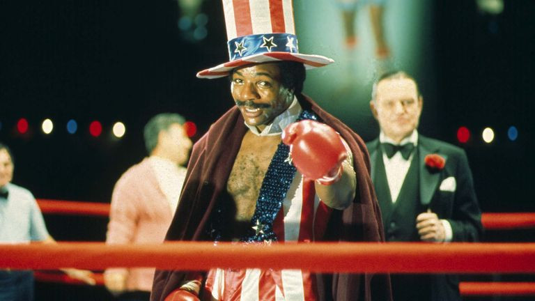 Carl Weathers as Apollo Creed. He has an Uncle Sam hat and outfit and is pointing with a boxing glove.