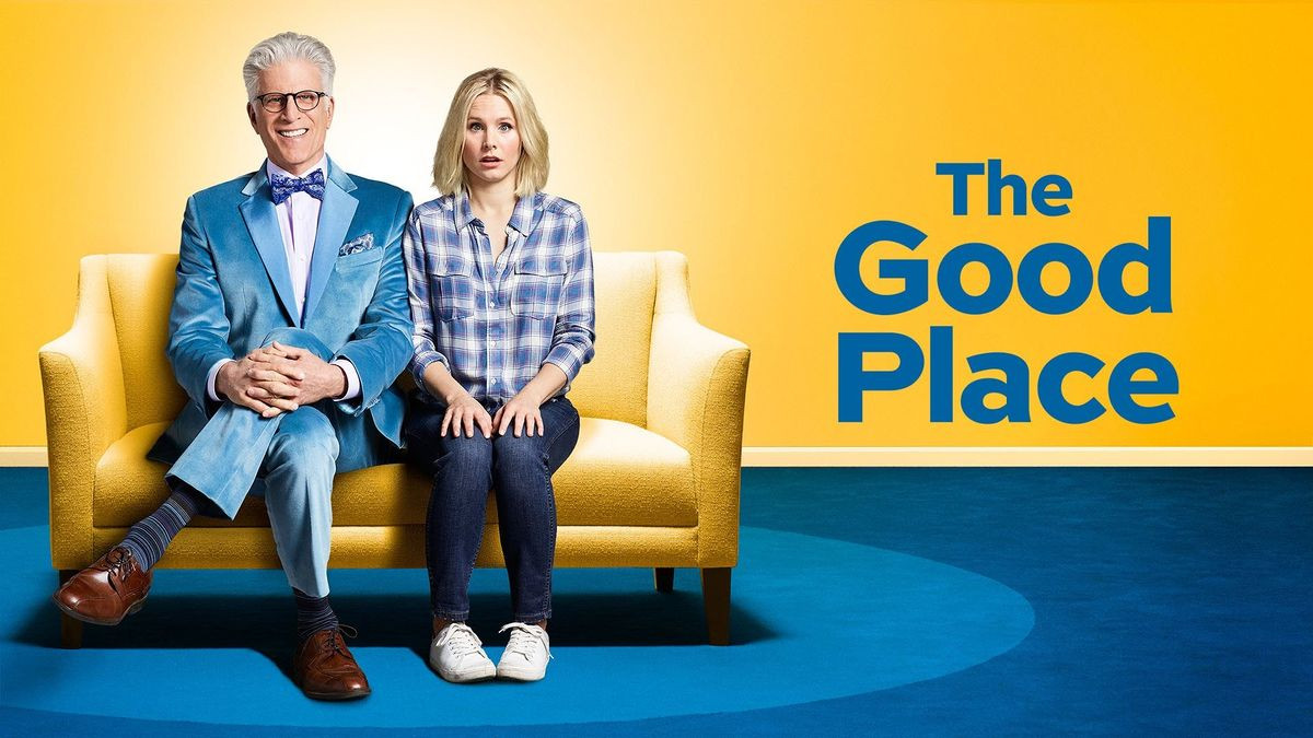 Elleanor y Michael, dos personajes de la obra coral 'the good place' sentados en un sofá amarillo. Michael está sonriendo, con las manos entrelazadas y las piernas cruzadas, sonriendo, y Elleanor mantiene las manos sobre las rodillas con gesto de sorpresa, sin tener mucha idea de lo que está pasando.