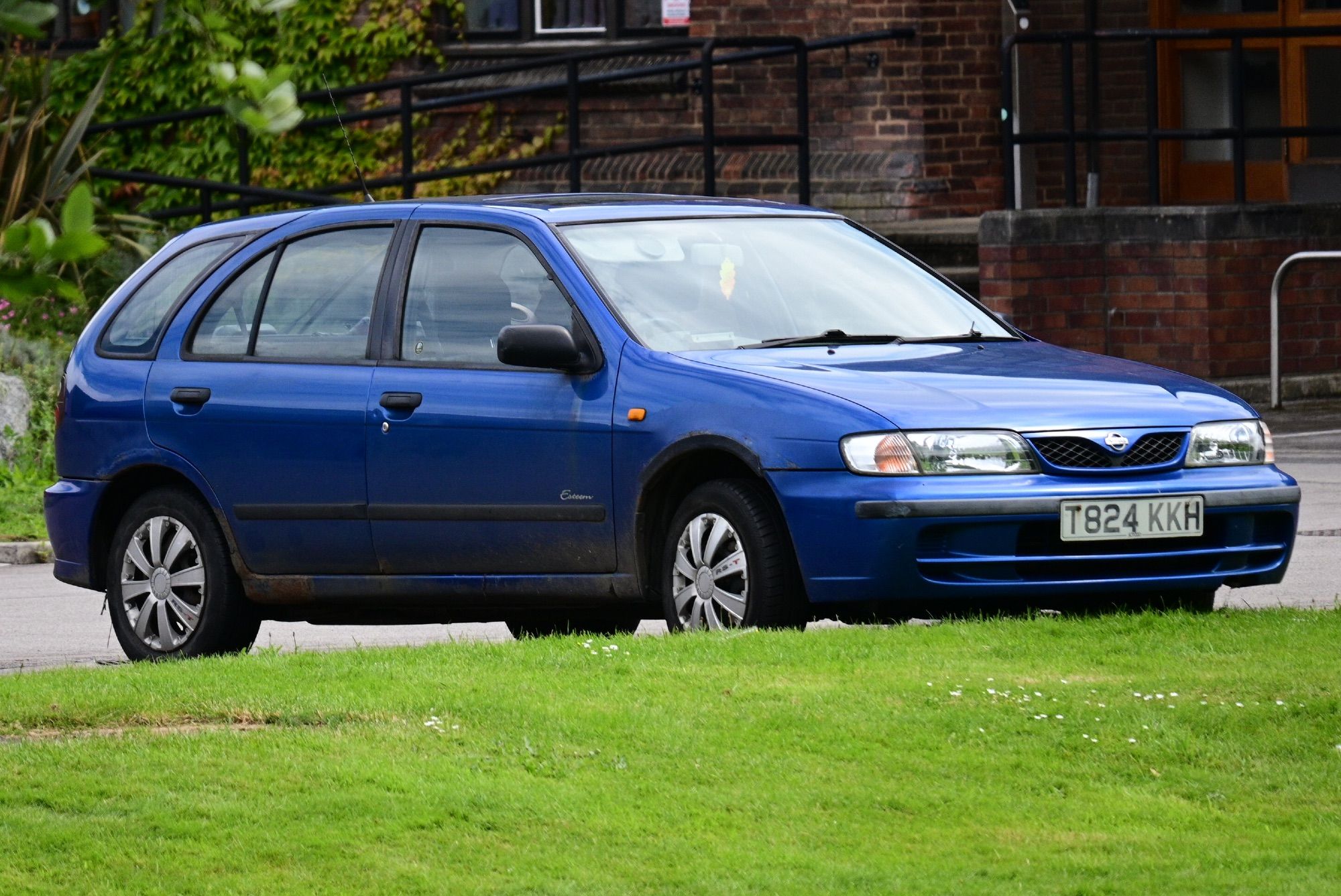 A blue and slightly rusty Toyota Almera Esteem estate parked in a public car park.