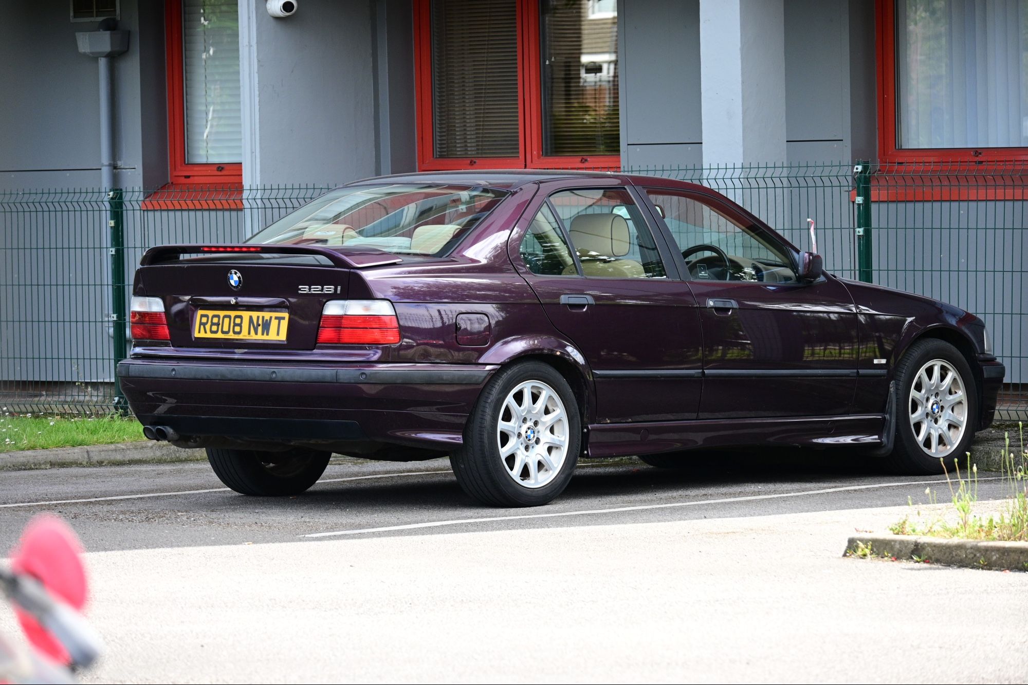 A purple BMW E36 328i sedan with spoiler and cream interior parked in a residential car park.