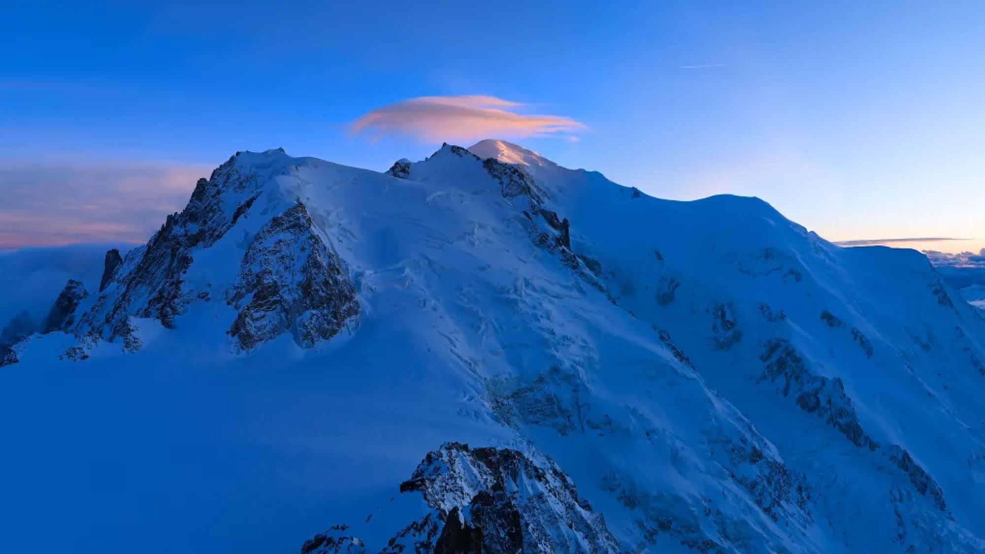 Vue sur le Mont Blanc au soleil couchant, dans une ambiance très bleutée, avec juste un nuage rose posé au-dessus de son sommet.