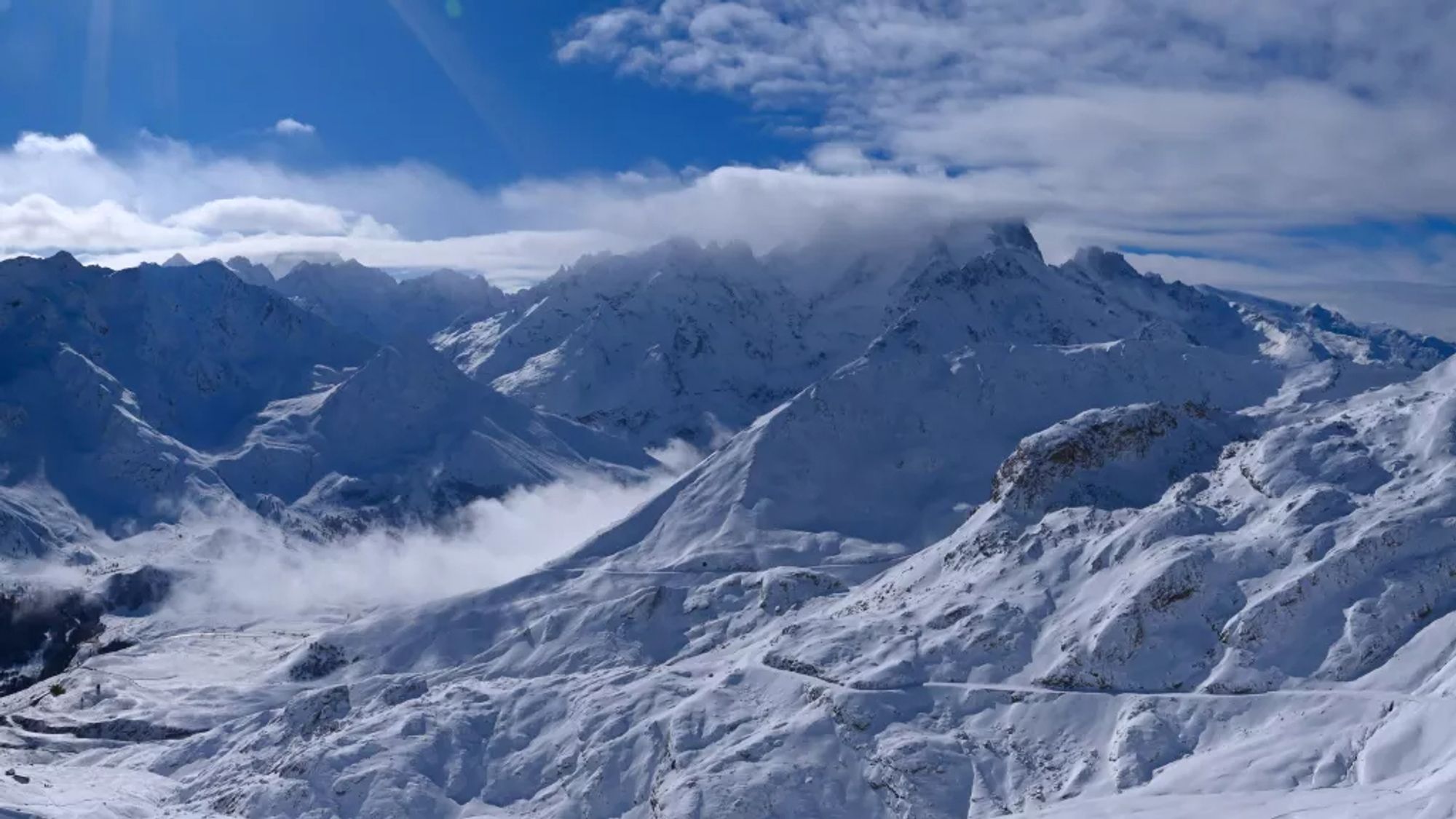 Montagnes enneigées, avec quelques nuages qui flottent sous un ciel bleu azur.