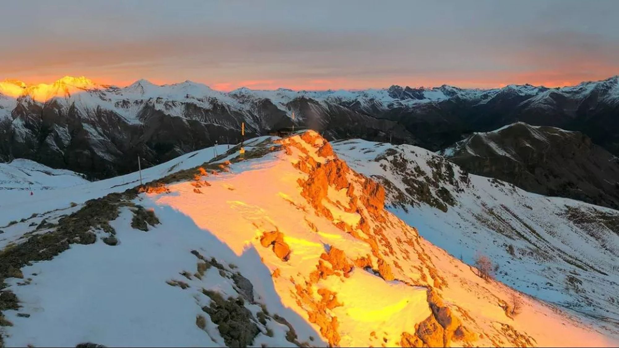 Soleil orangé sur un sommet enneigé, dans une ambiance grisâtre.