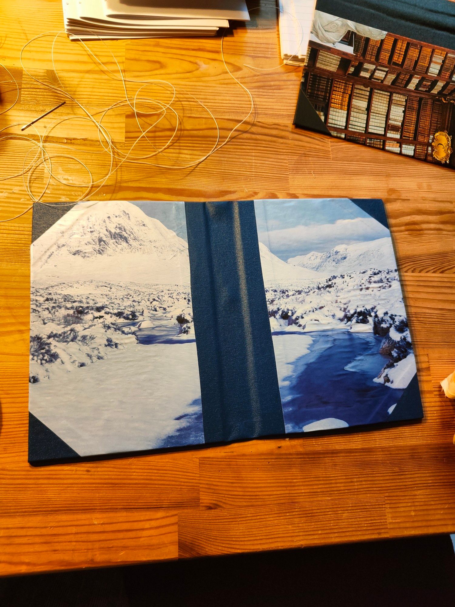 Selbstgemachter Buchumschlag der auf einem Holztisch liegt. Blaue Leinen und das bild zeigt einen Berg Fluss und einen eine Landschaft mit Schnee