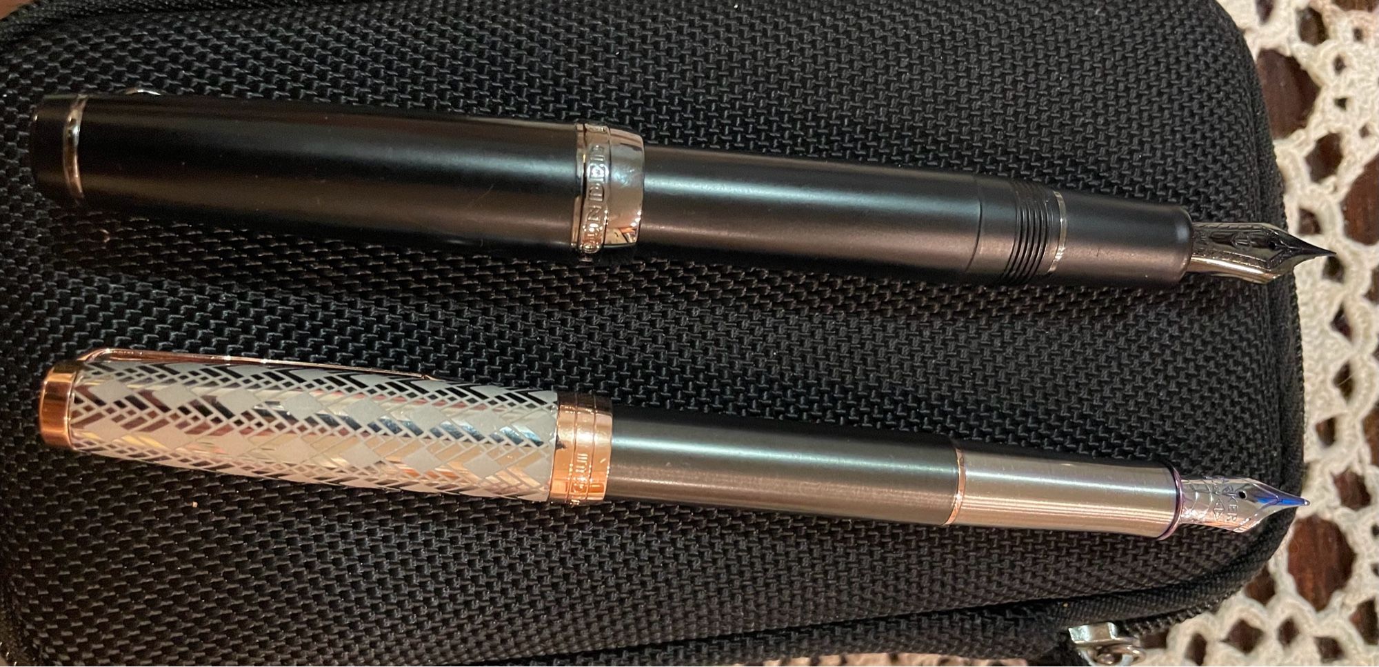 Two mounted fountain pens on black case. One is a Parker pen —sliver, grey, and red. The other is a black Sailor pen with gold trim.