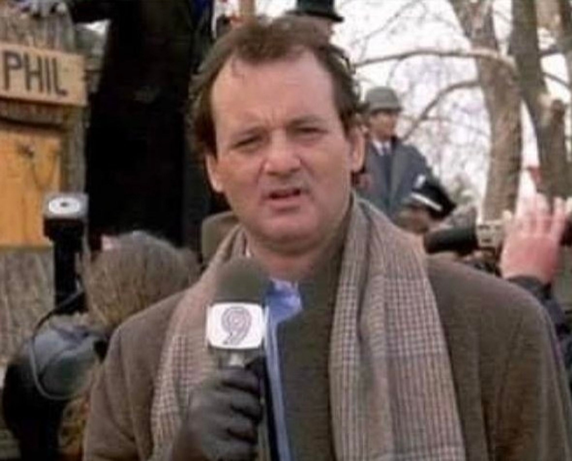 Bill Murray als Wettermann Phil Connors in dem Film und täglich grüßt das Murmeltier, er steht am Groundhog Day mit einem Mikrofon in der Hand und genervtem Blick unter anderen Reportern vor der Bühne, auf der Phil das Murmeltier das Wetter der kommenden Wochen vorhersagen soll.