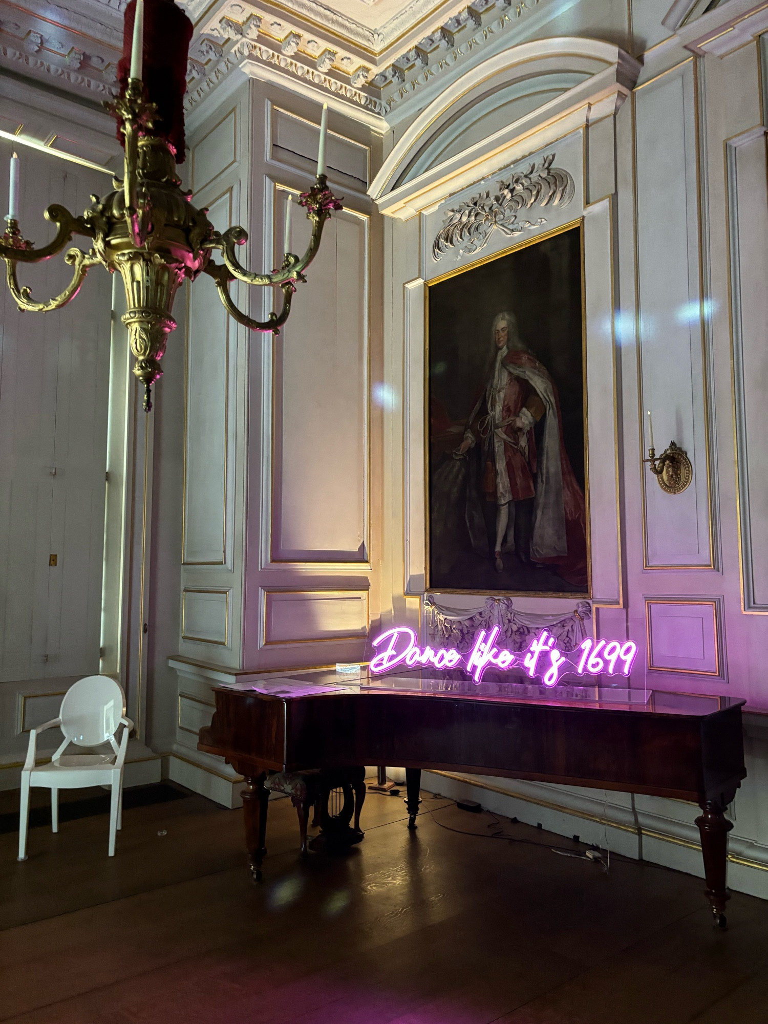 A piano with the phrase dance like it’s 1699 in a stately room with white walls and chandelier.